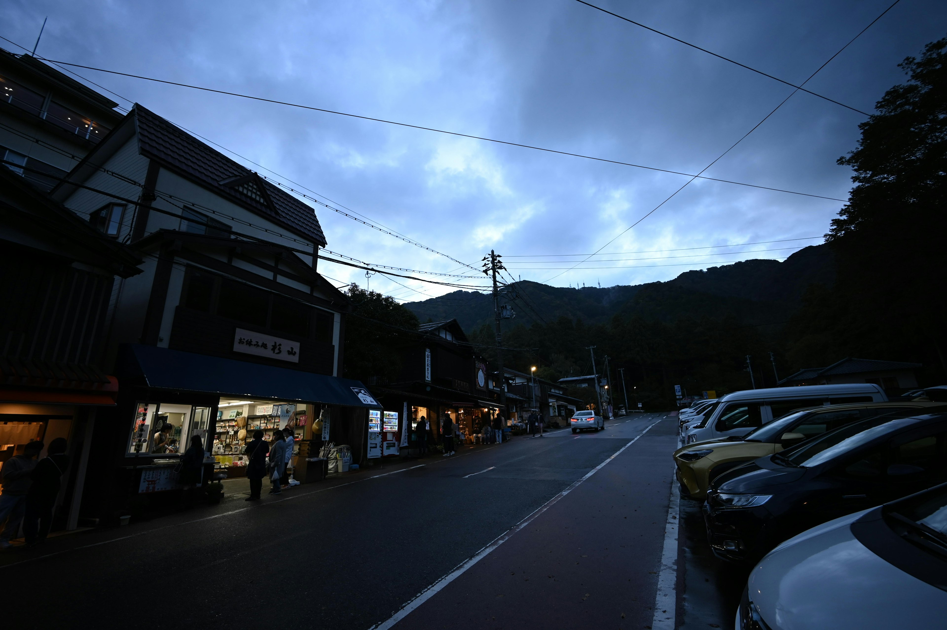 Scène de rue sombre près des montagnes avec des voitures garées et des magasins