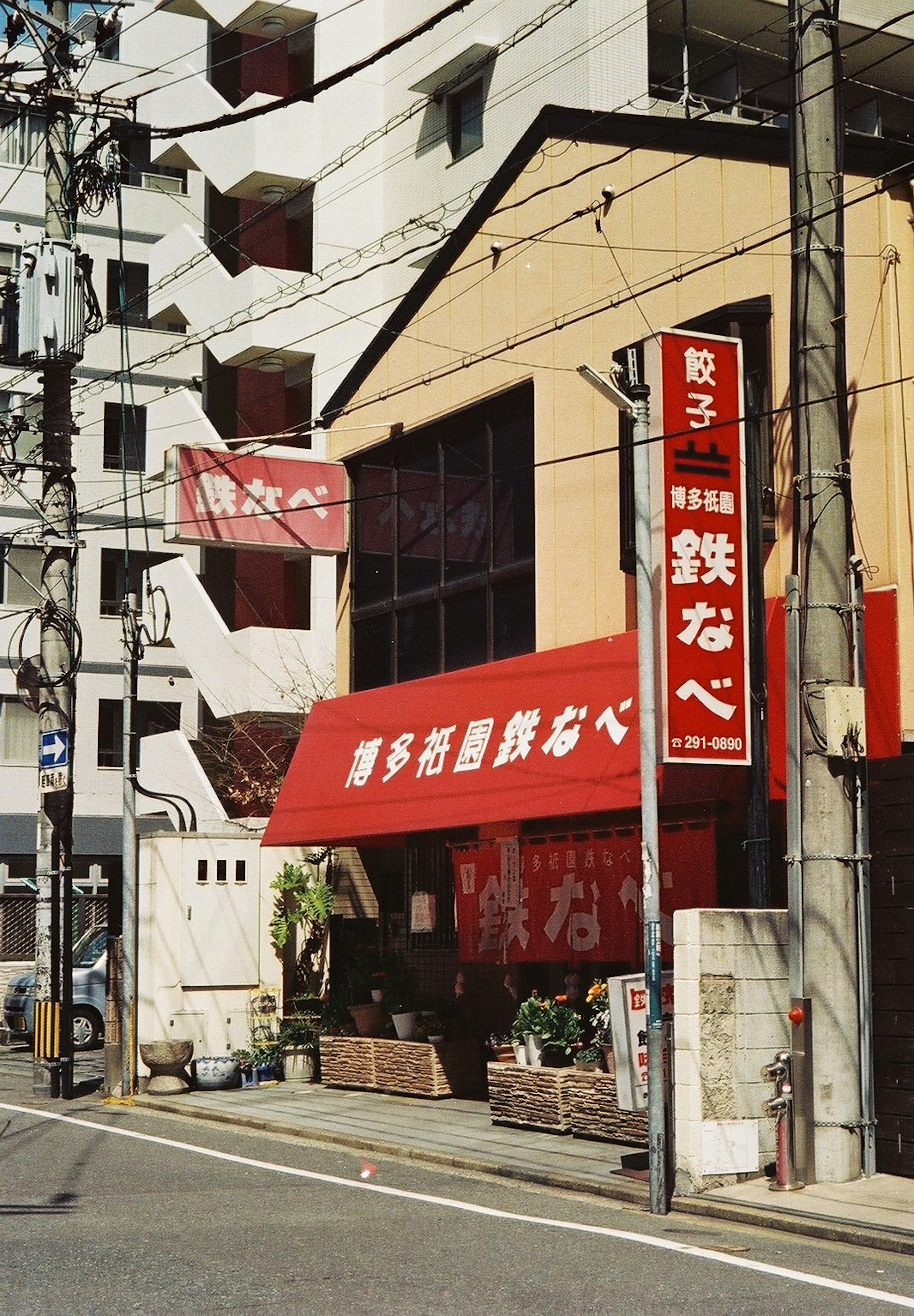 Exterior of a teppanyaki restaurant with a red awning plants in front and signage