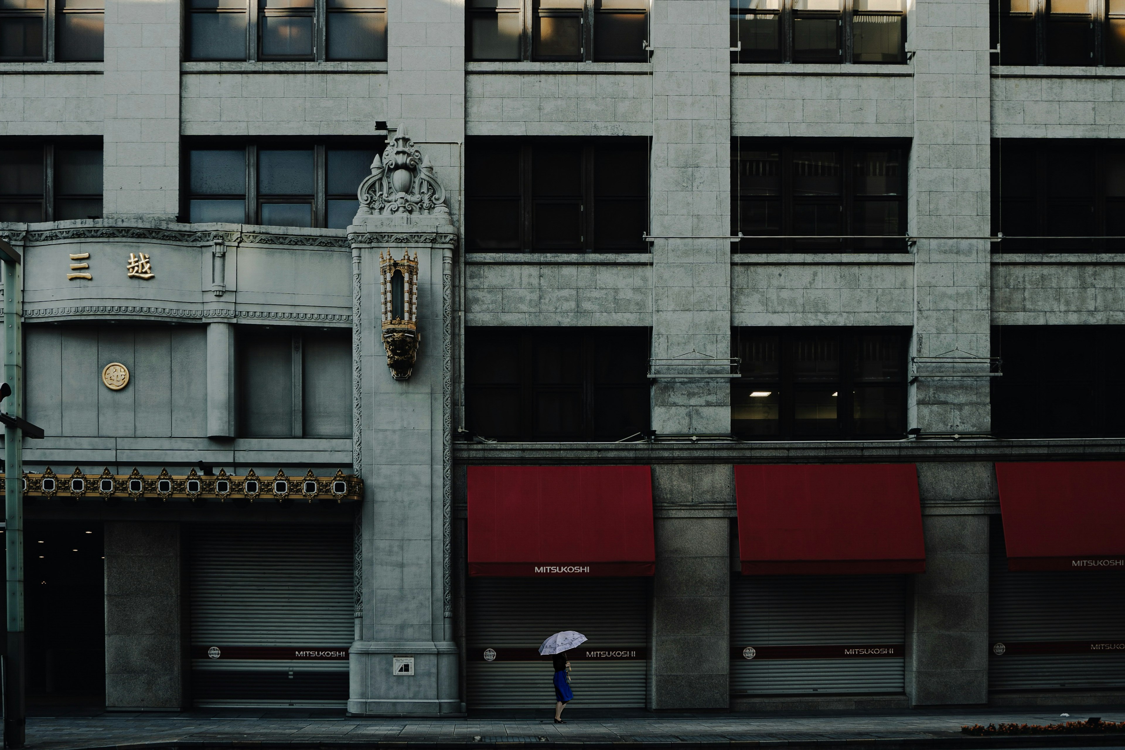 Street scene featuring a person with an umbrella under a red awning and an old building facade