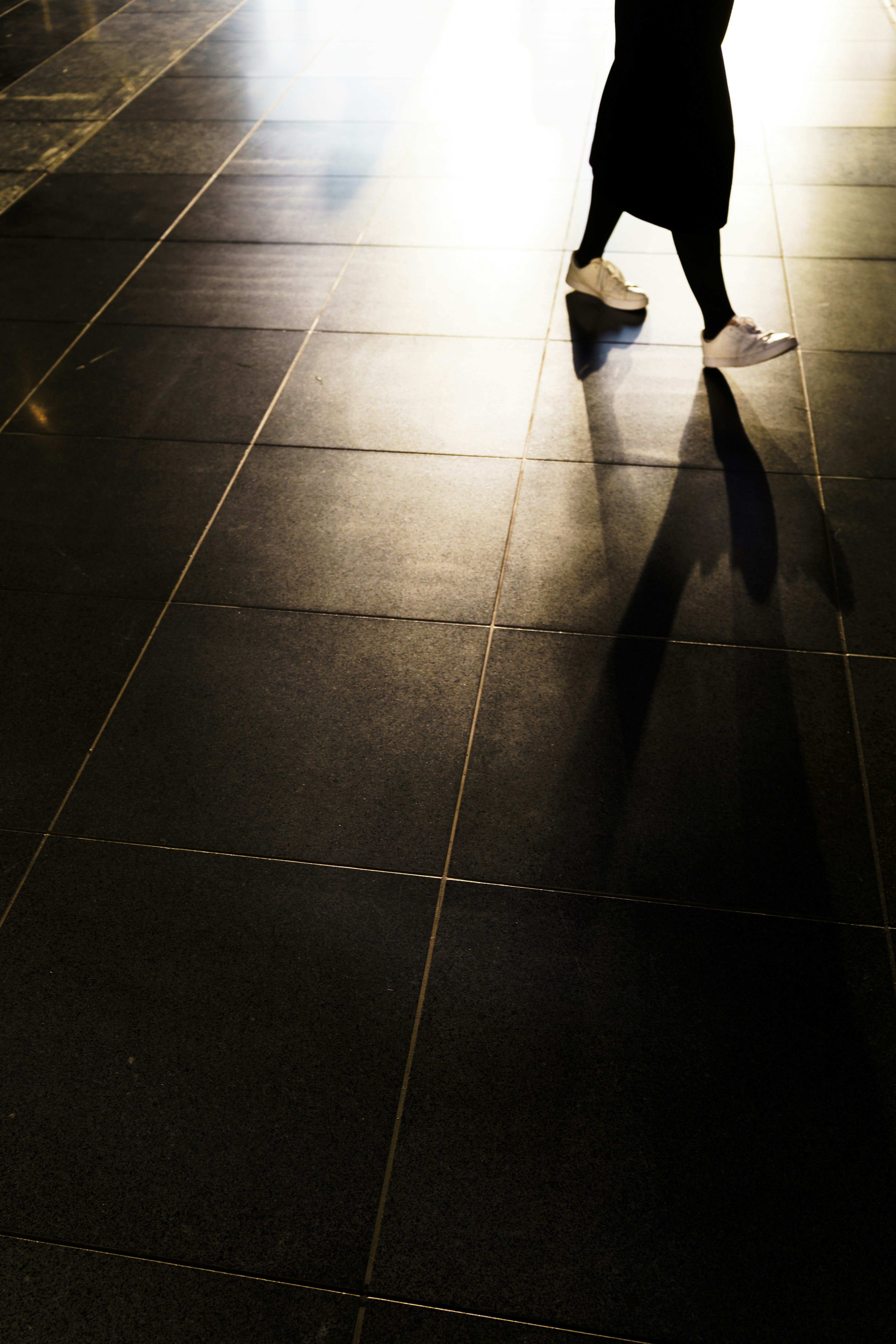 Una persona che cammina su un pavimento in piastrelle nere proiettando un'ombra lunga