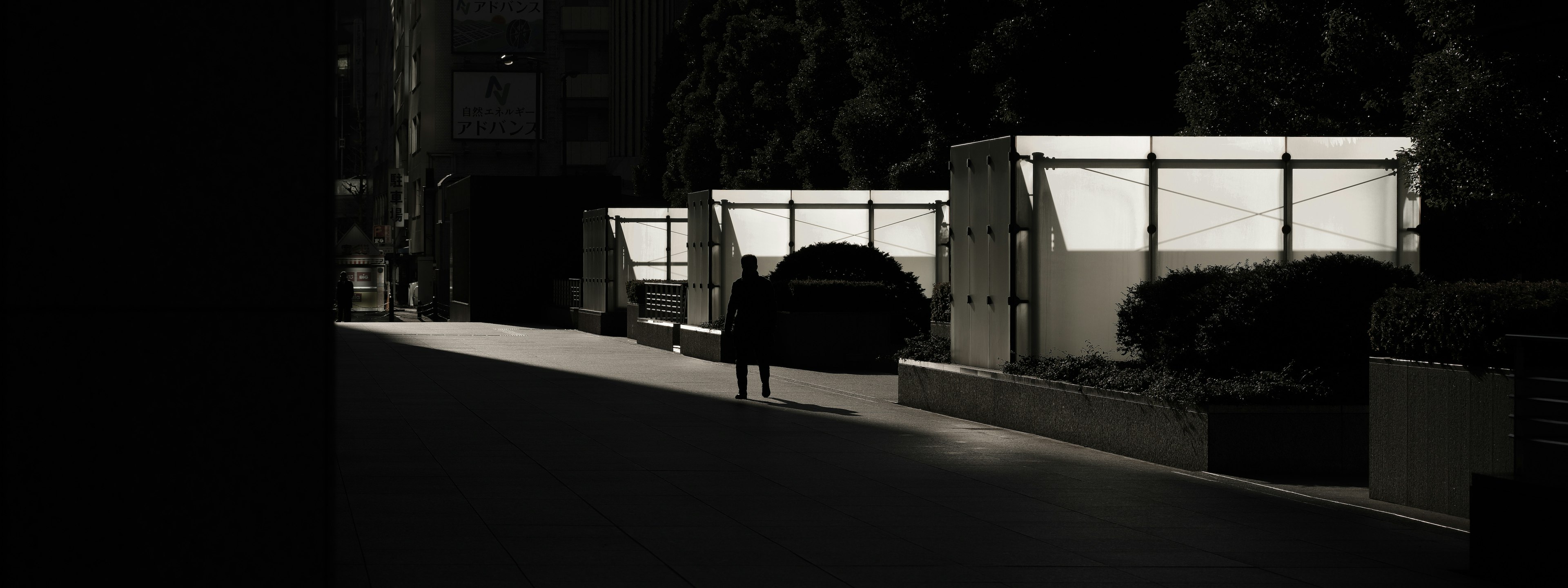 Silhouette di una persona su una strada buia con tende illuminate