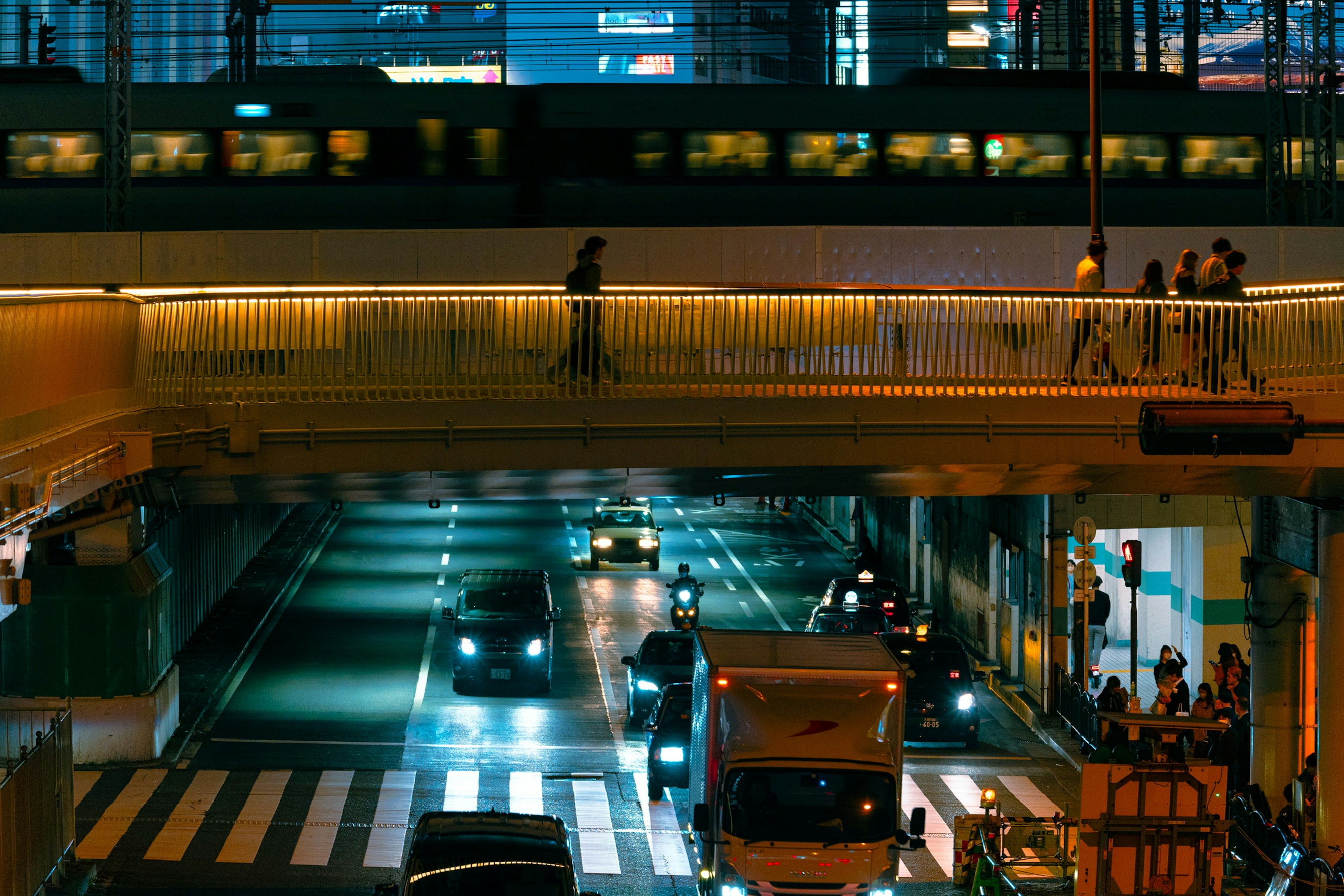 Paisaje urbano nocturno con un puente peatonal y vehículos debajo