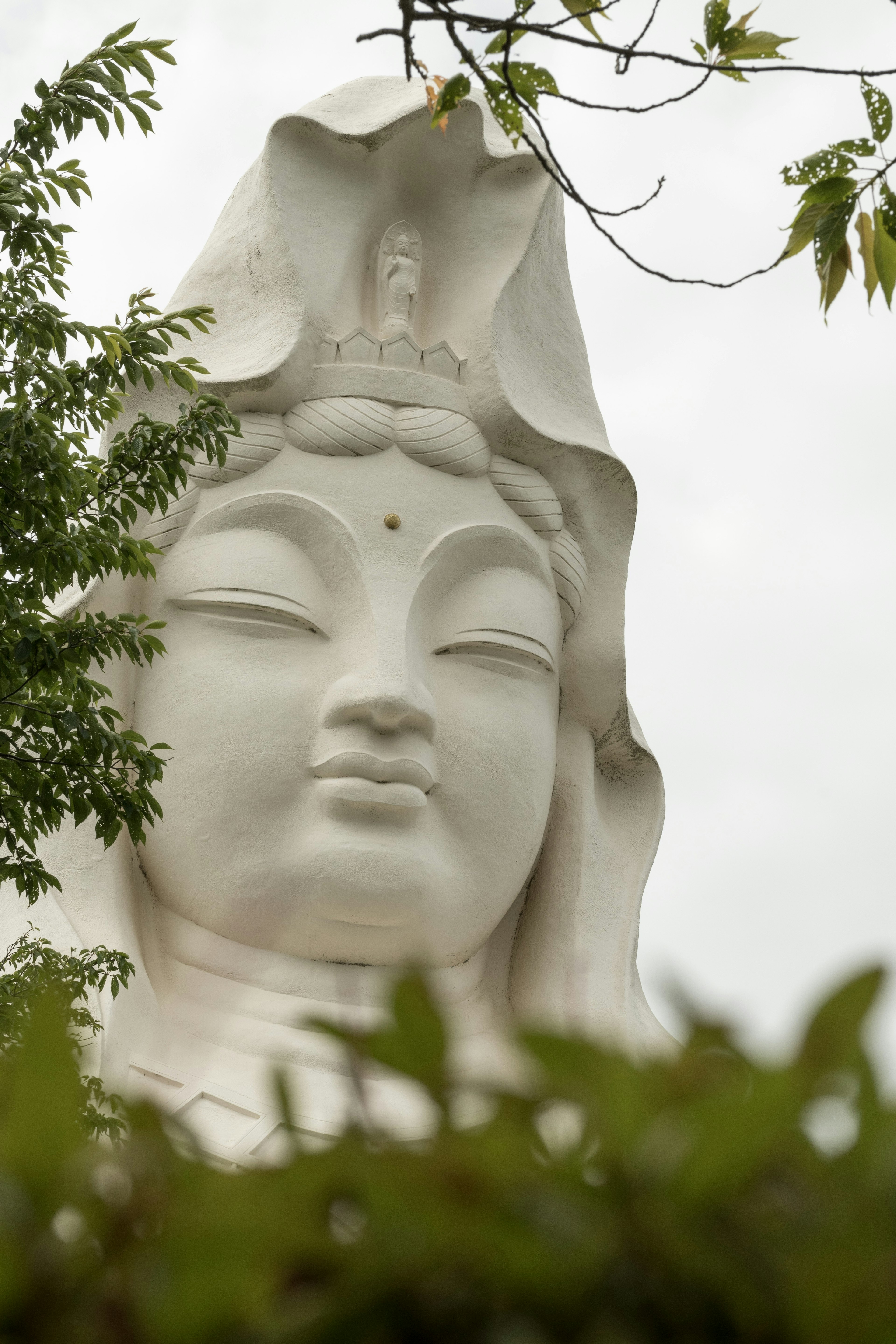 Close-up of a serene white Kannon statue partially surrounded by green foliage