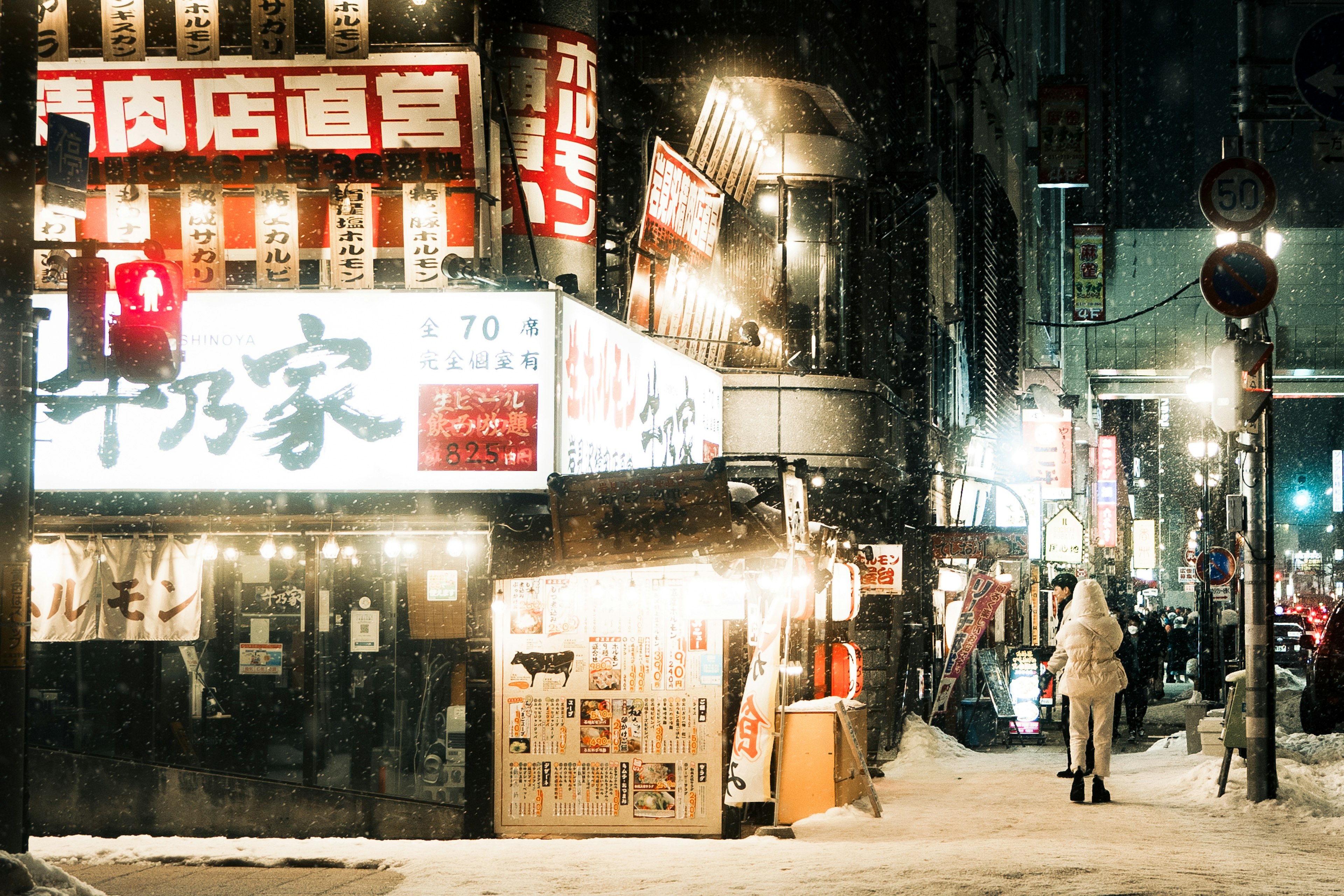 Escena nocturna nevada en Japón con letreros de restaurantes y peatones