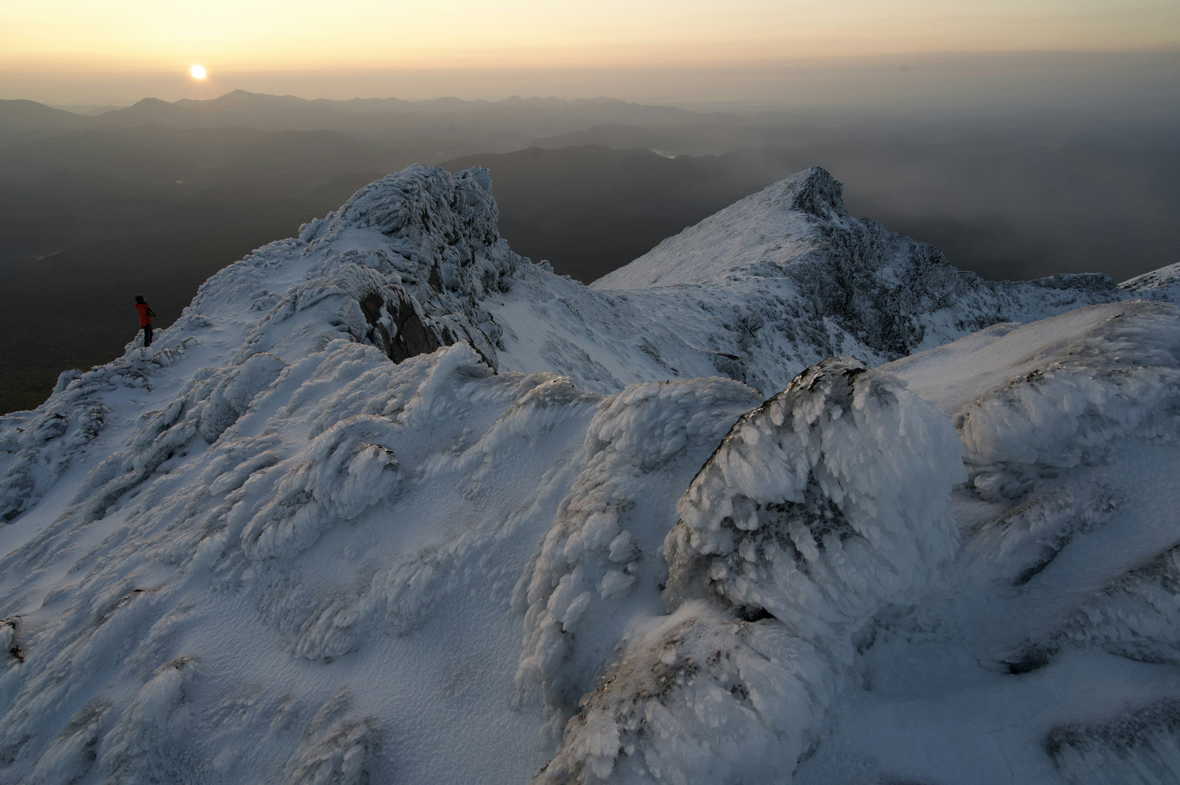 Silhouette eines Kletterers auf einem schneebedeckten Berggipfel mit Sonnenuntergang im Hintergrund