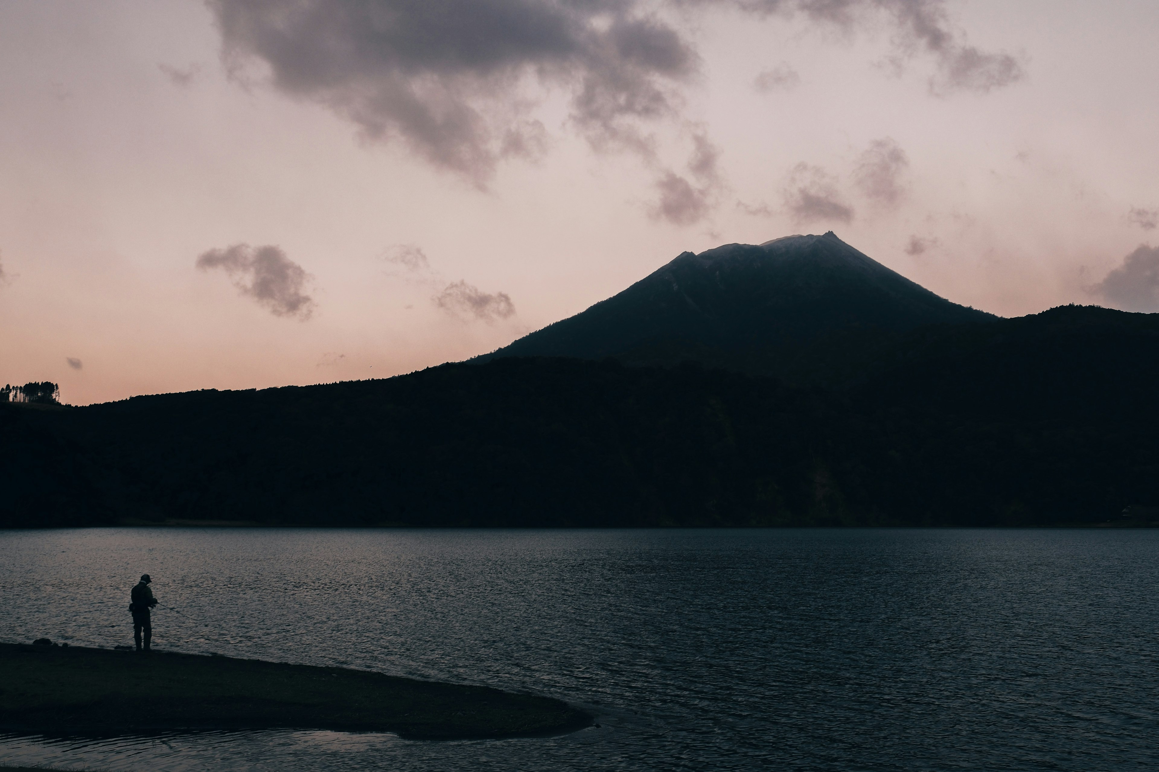 Silhouette d'une personne au bord d'un lac avec une montagne au crépuscule