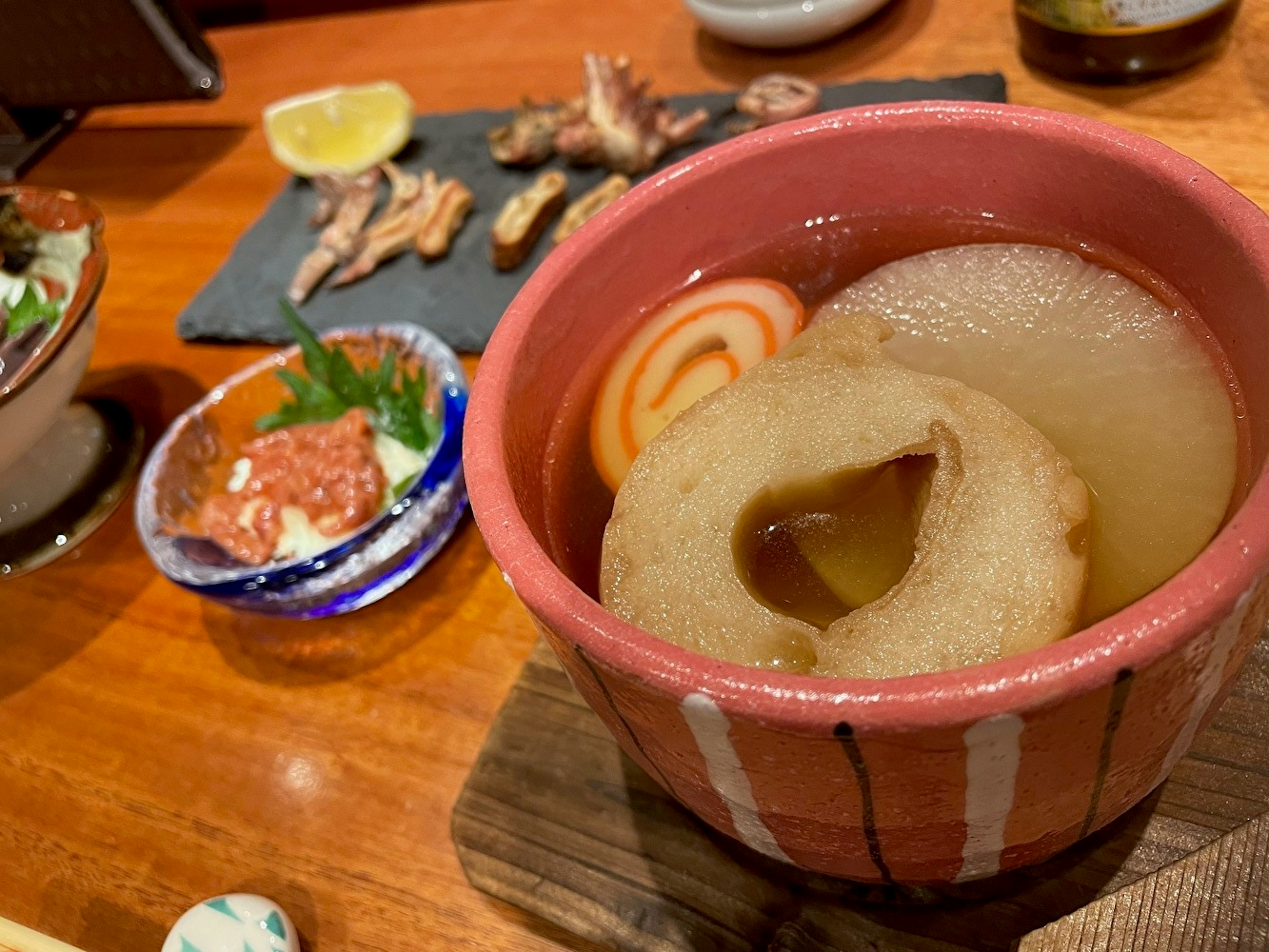 Eine Schüssel japanischer Suppe mit Radieschenscheiben und dekorativen Fischkuchen neben einem Teller mit verschiedenen Gerichten