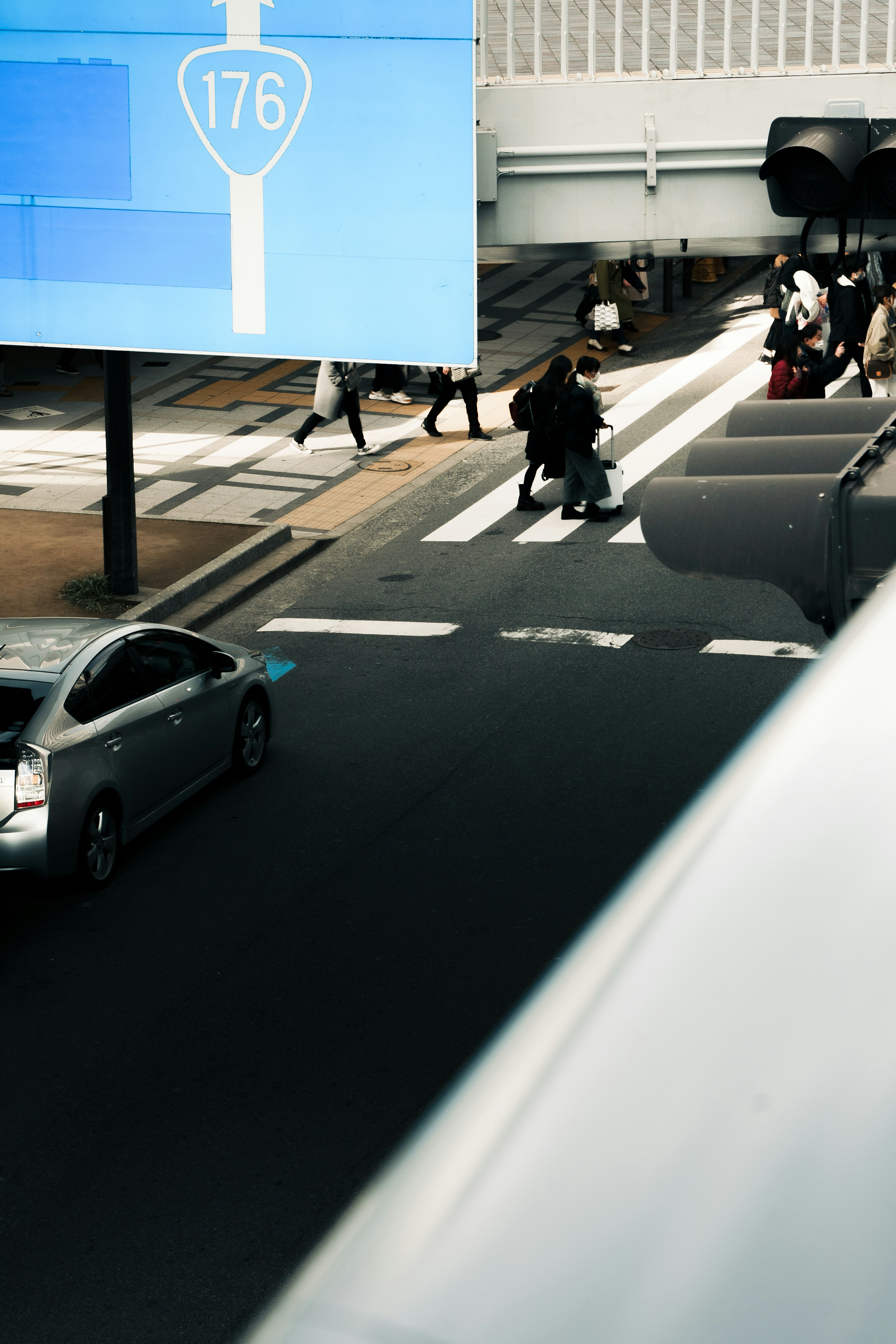 青い看板の下を歩く人々と通行車両が見える都市の交差点