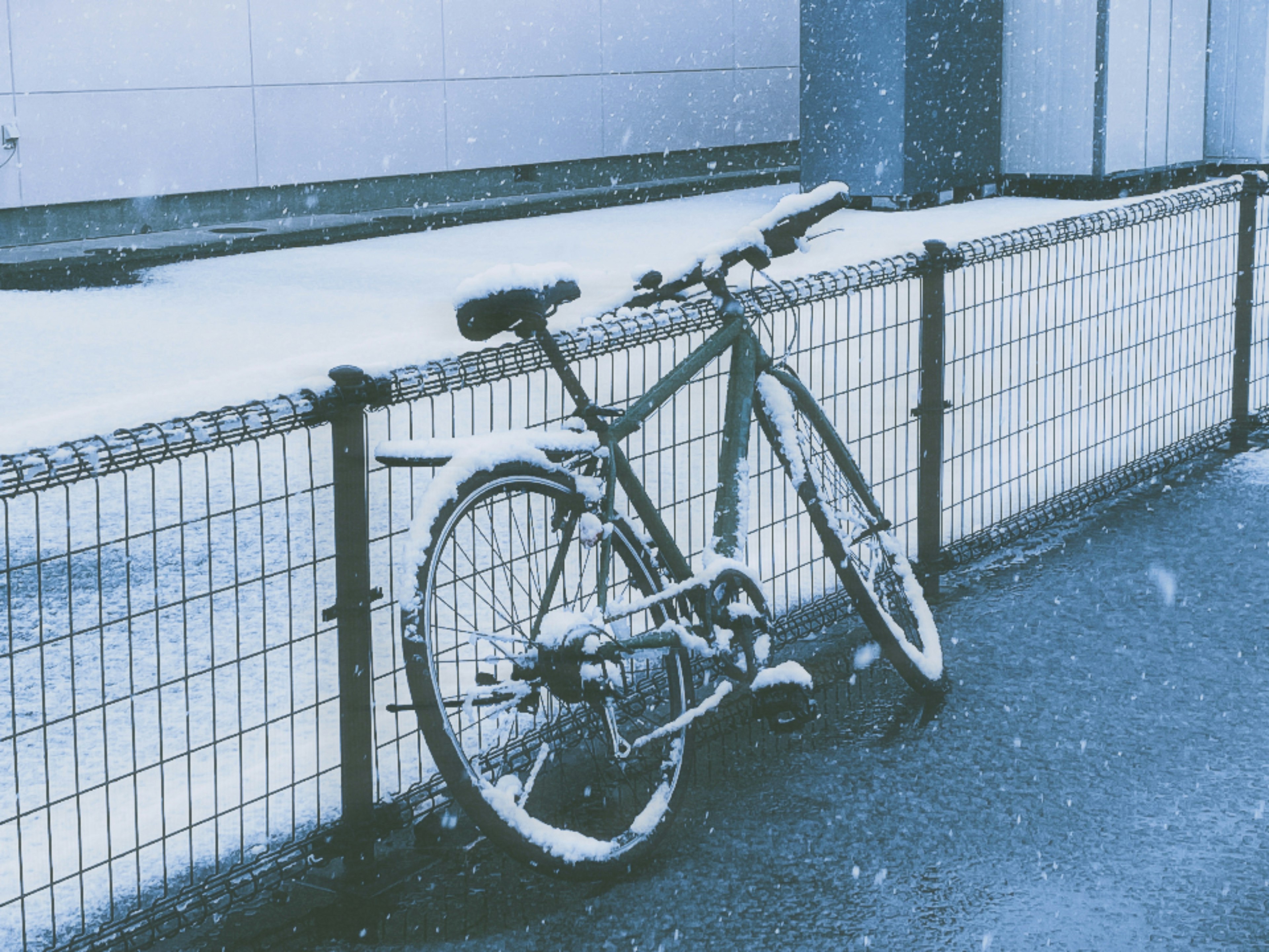 Bicycle covered in snow leaning against a fence