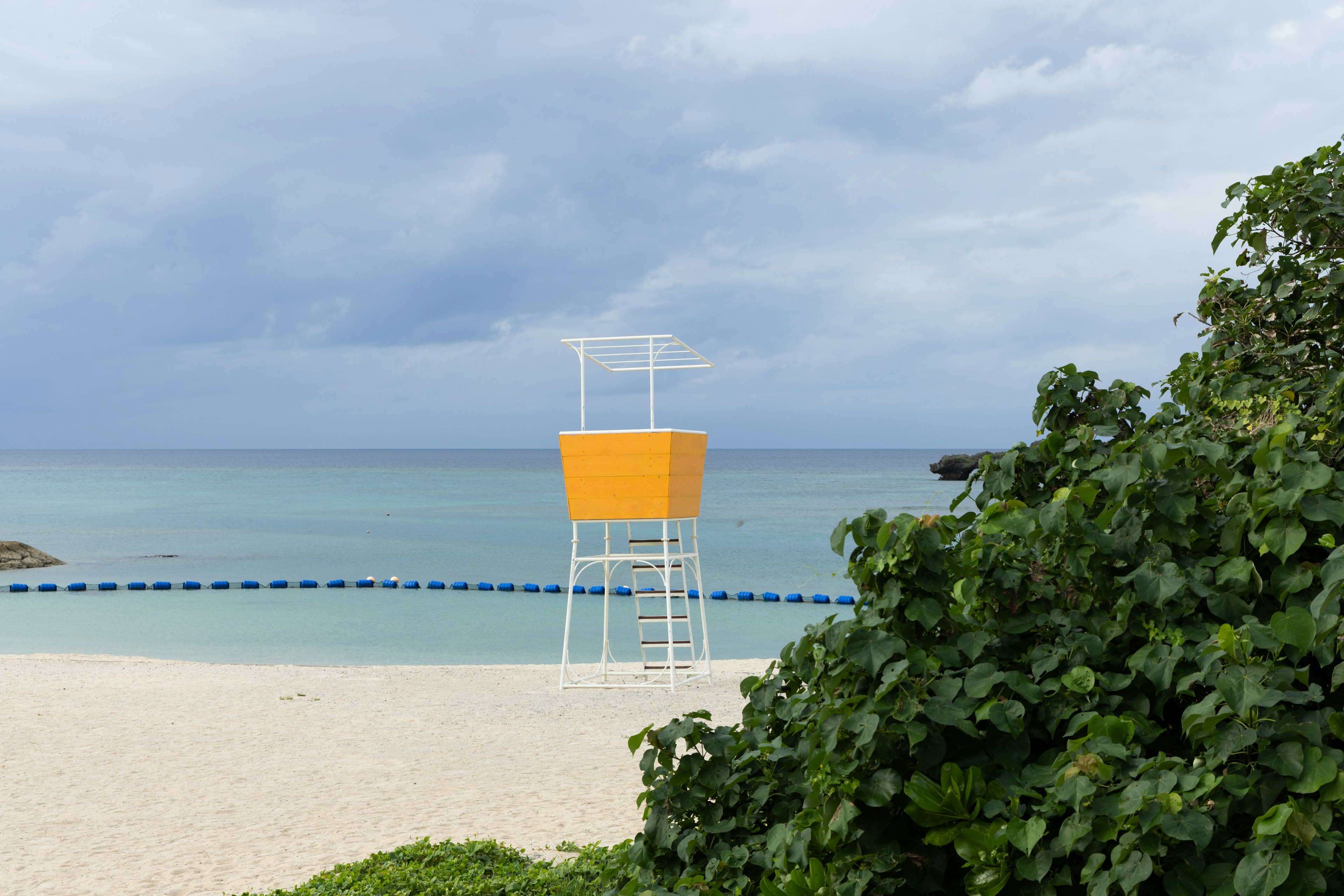 ฉากชายหาดที่มีหอคอยชีวิตสีเหลืองอยู่หน้าทะเลสีน้ำเงิน