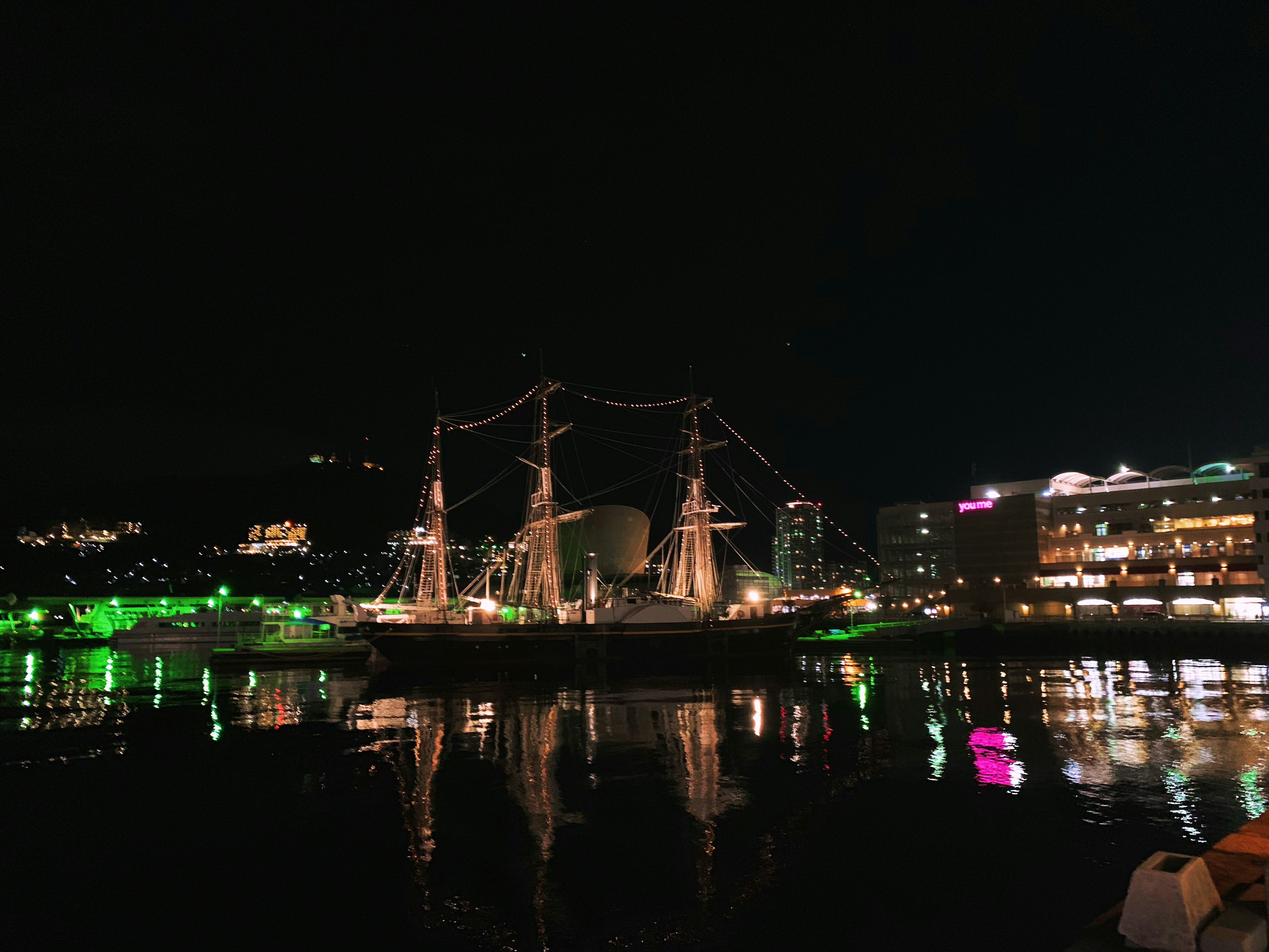 Ein beleuchtetes Segelschiff bei Nacht mit Spiegelungen im Wasser