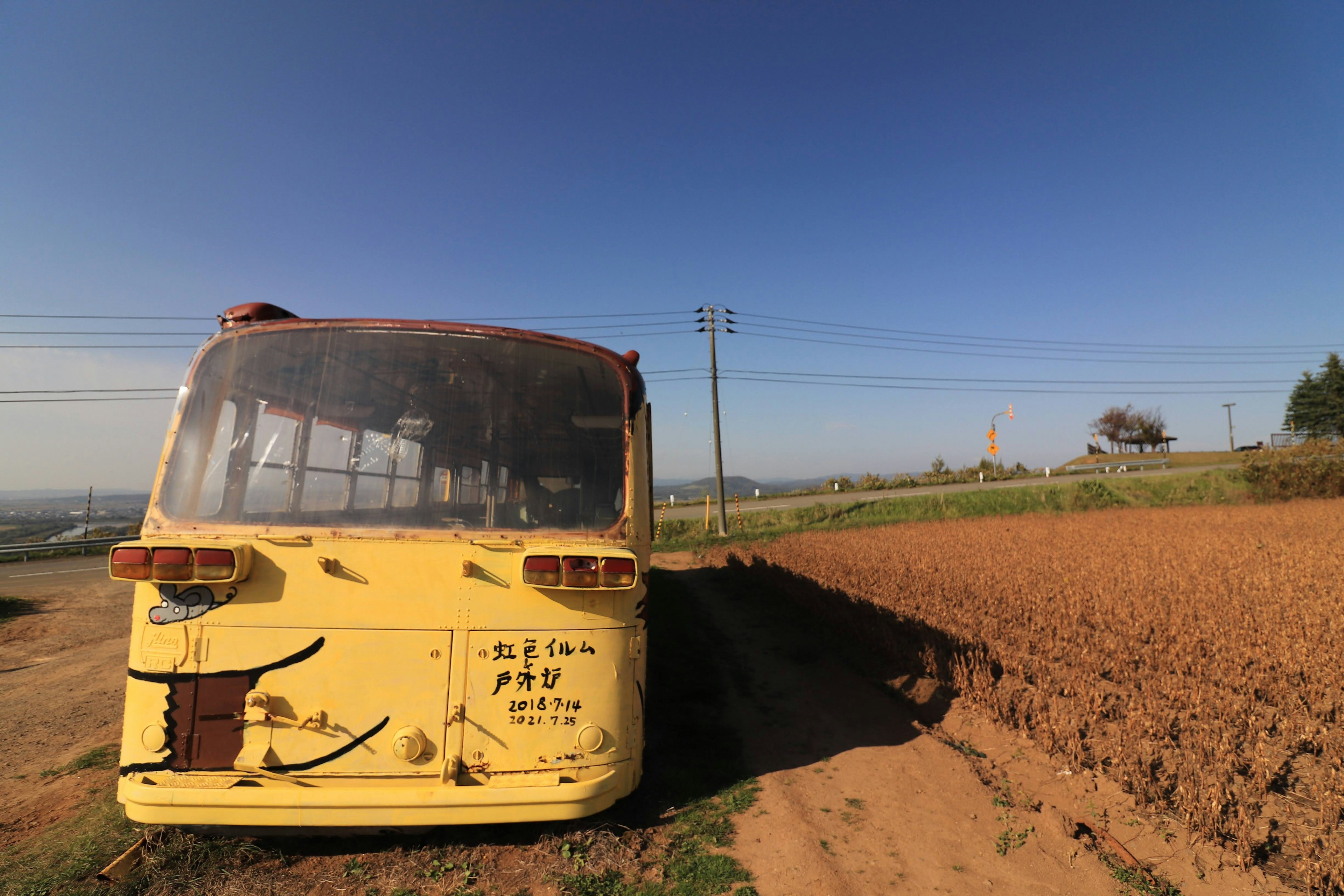 Sebuah bus kuning tua diparkir dekat pemandangan lahan pertanian