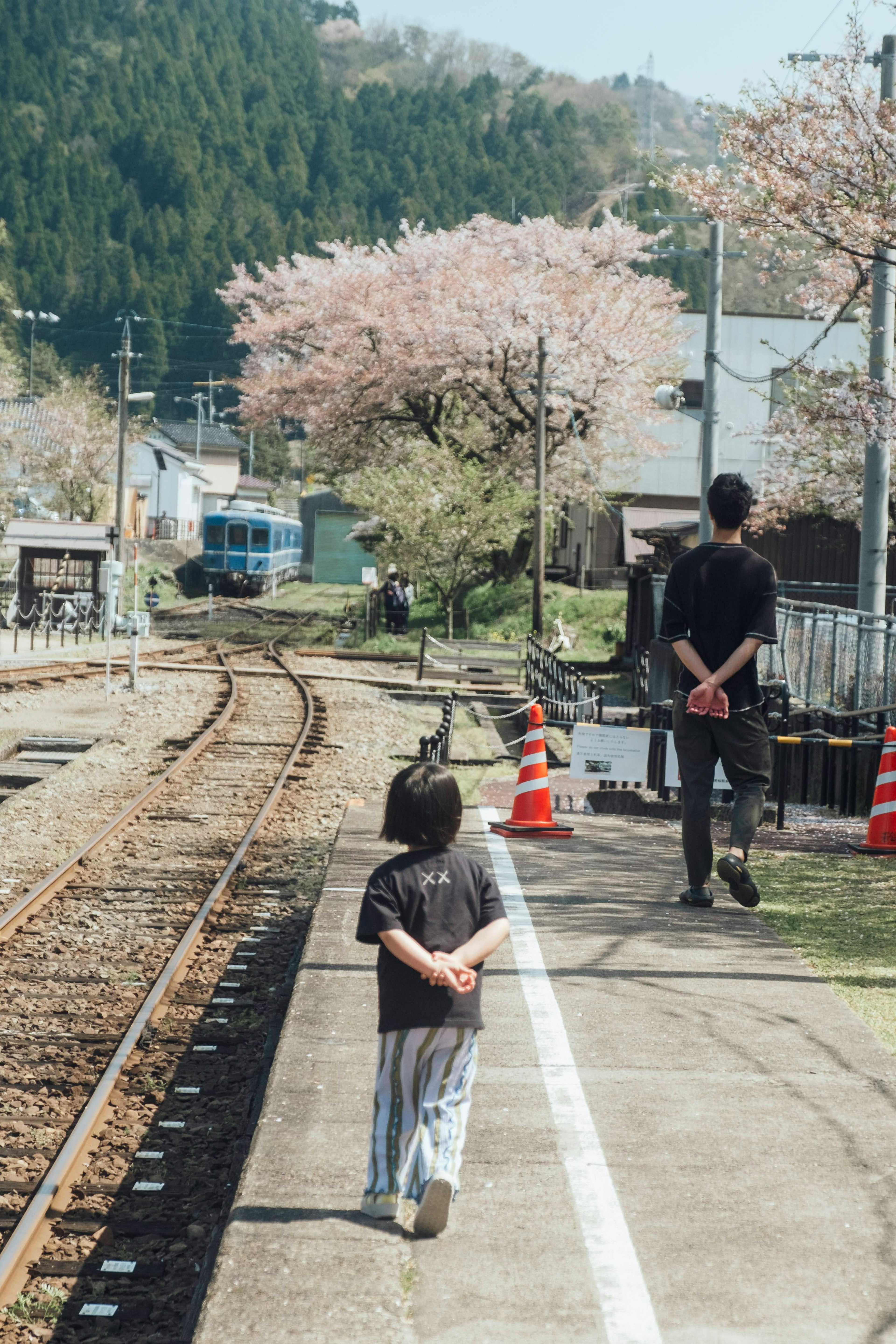 桜の木のある駅で子供と大人が歩いている風景