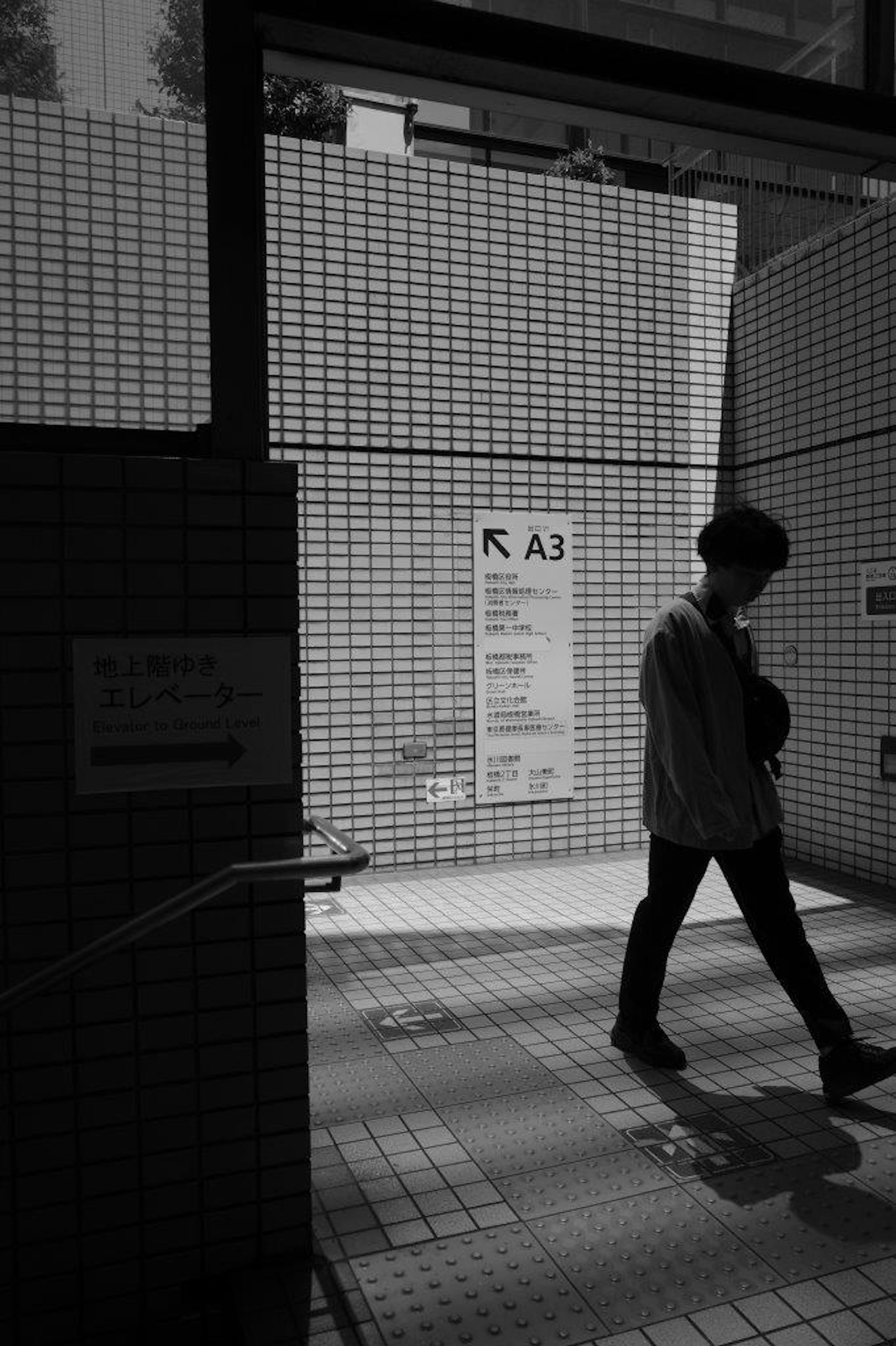 High-contrast black and white urban scene with a person walking in front of a message board