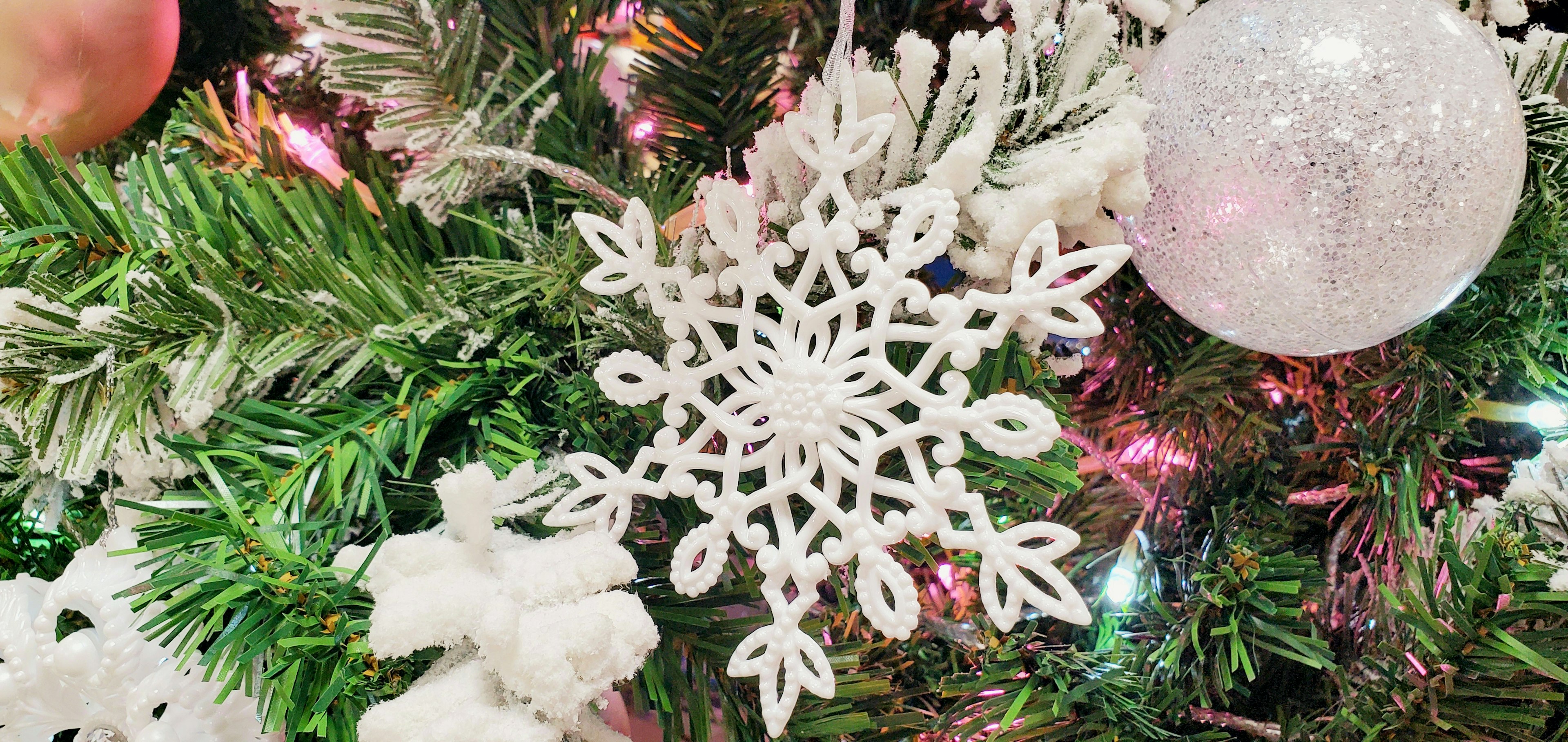 Ornamento a forma di fiocco di neve bianco su un albero di Natale con decorazioni colorate