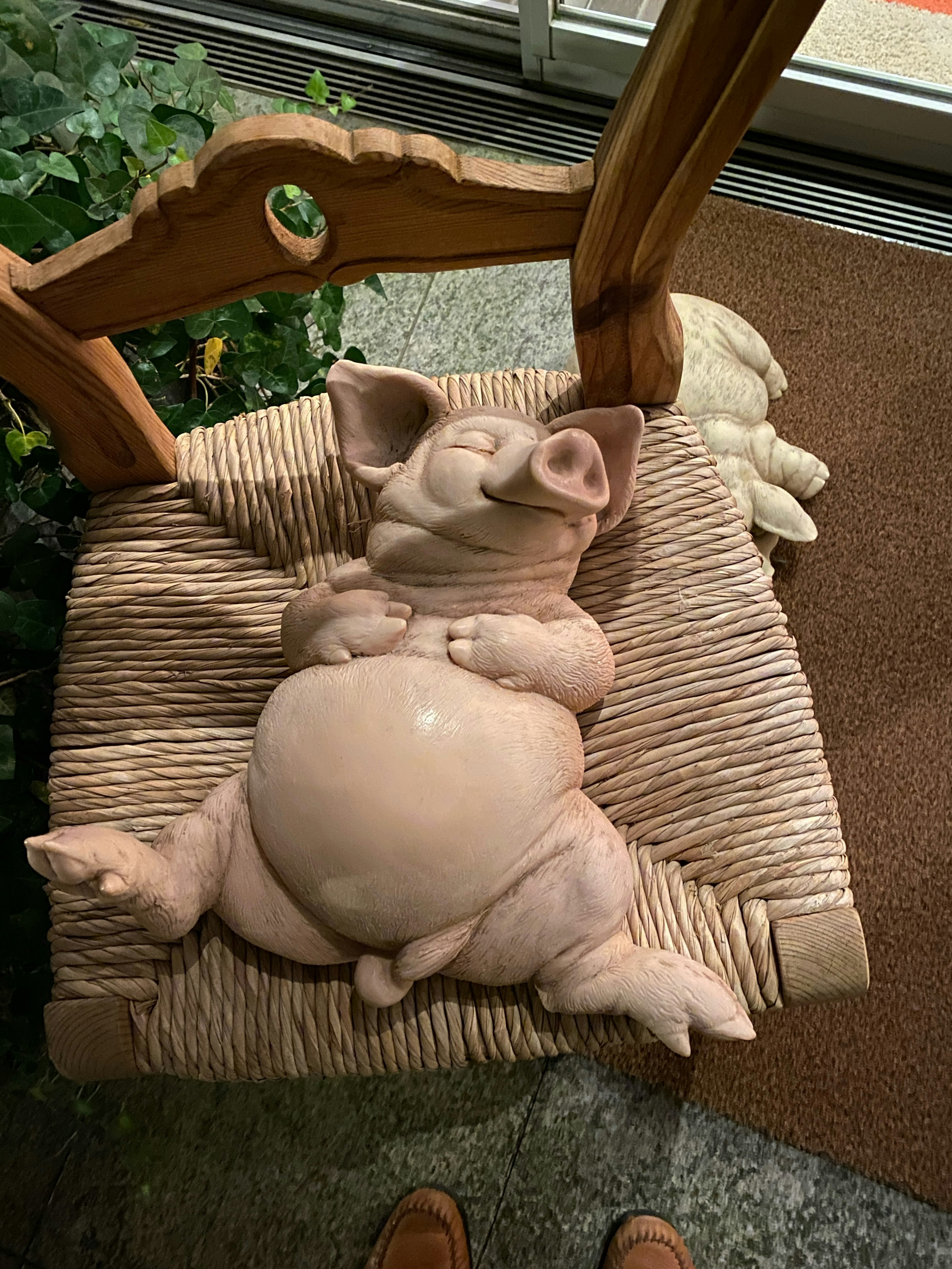 Una scultura di maiale in ceramica che si rilassa su una sedia in vimini