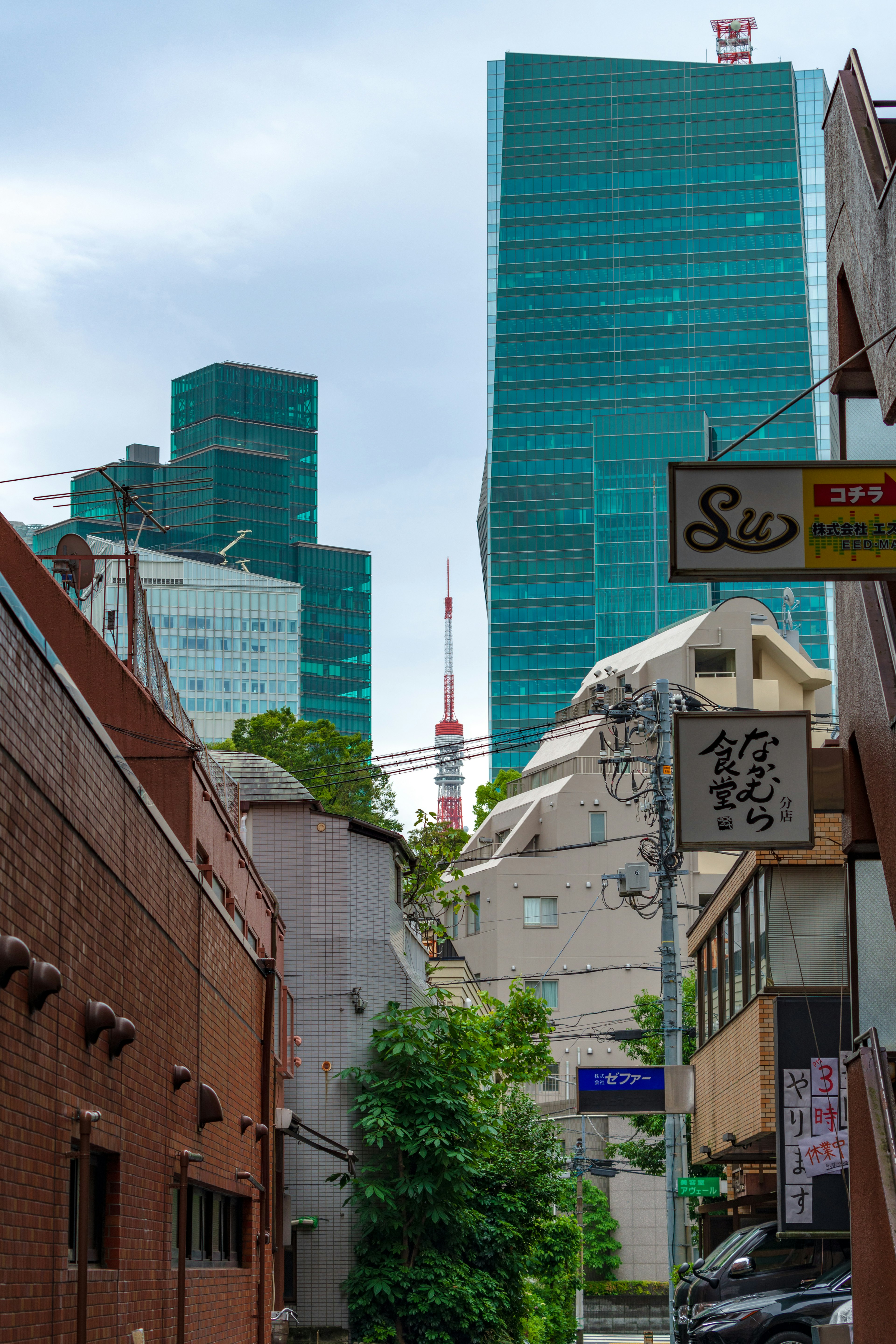 Urban landscape featuring Tokyo Tower visible among high-rise buildings and narrow alley