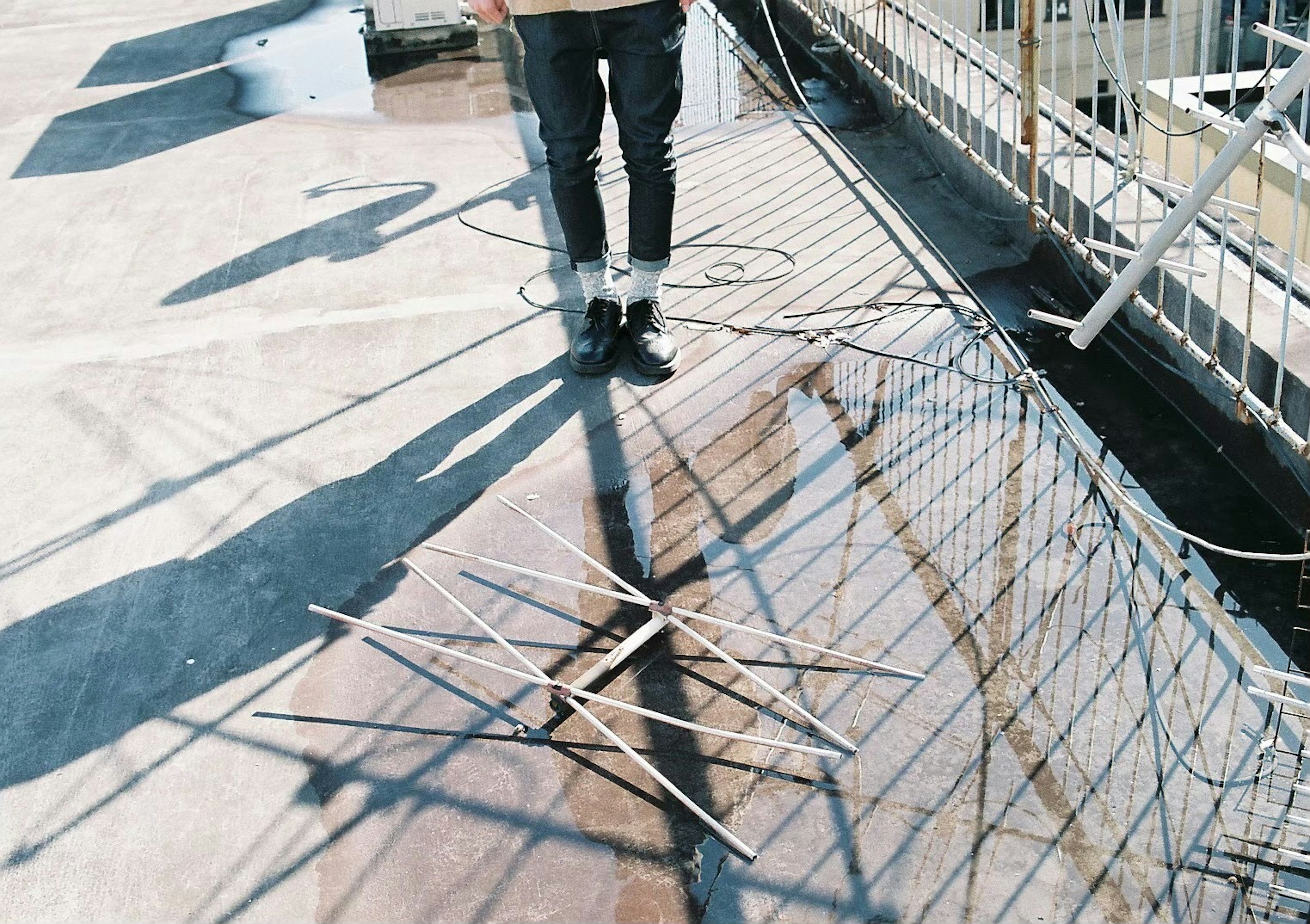 A person standing on a rooftop casting a shadow with wooden sticks on the ground