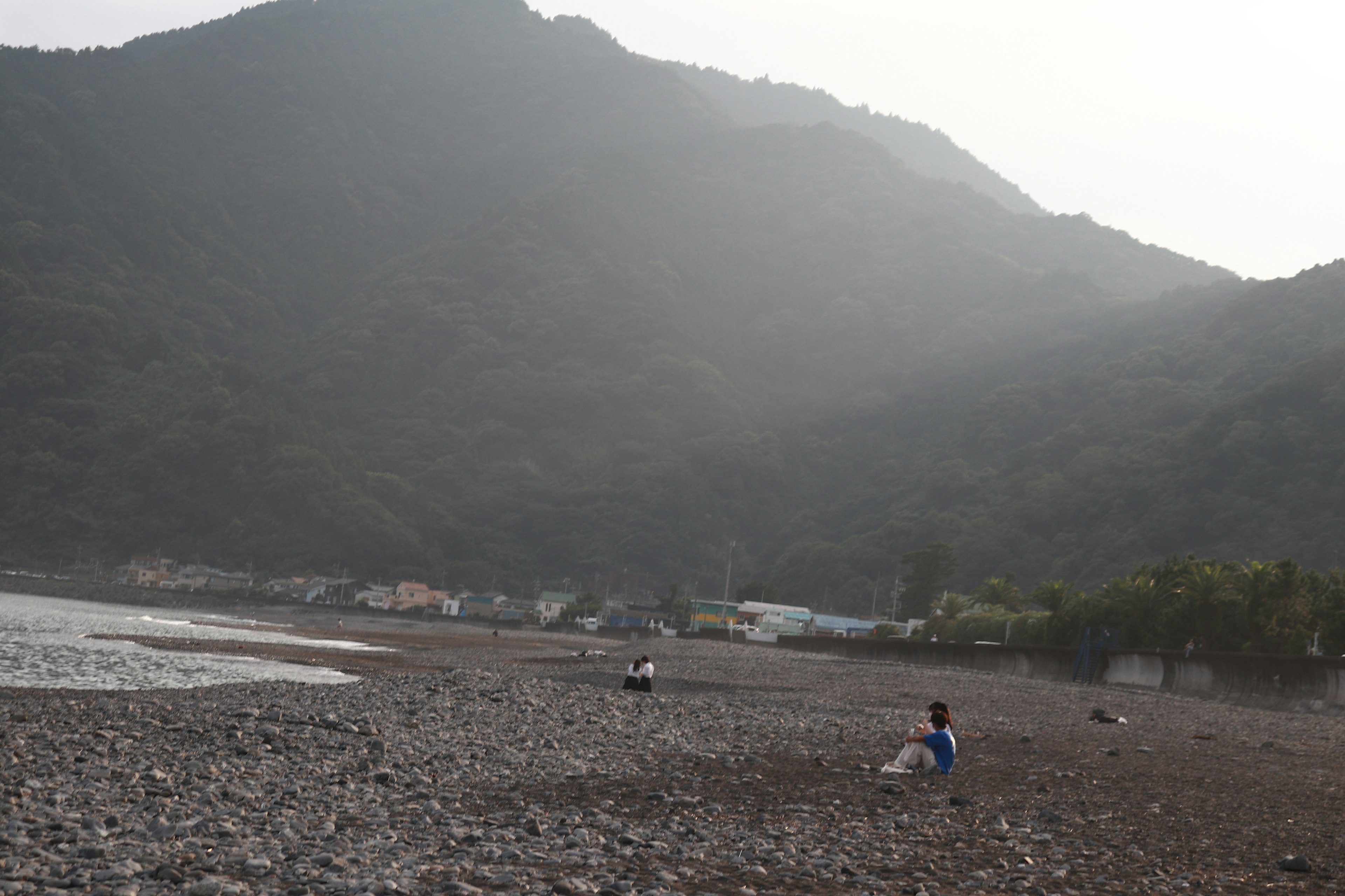 Steinstrand mit Bergen im Hintergrund und Menschen, die sich entspannen