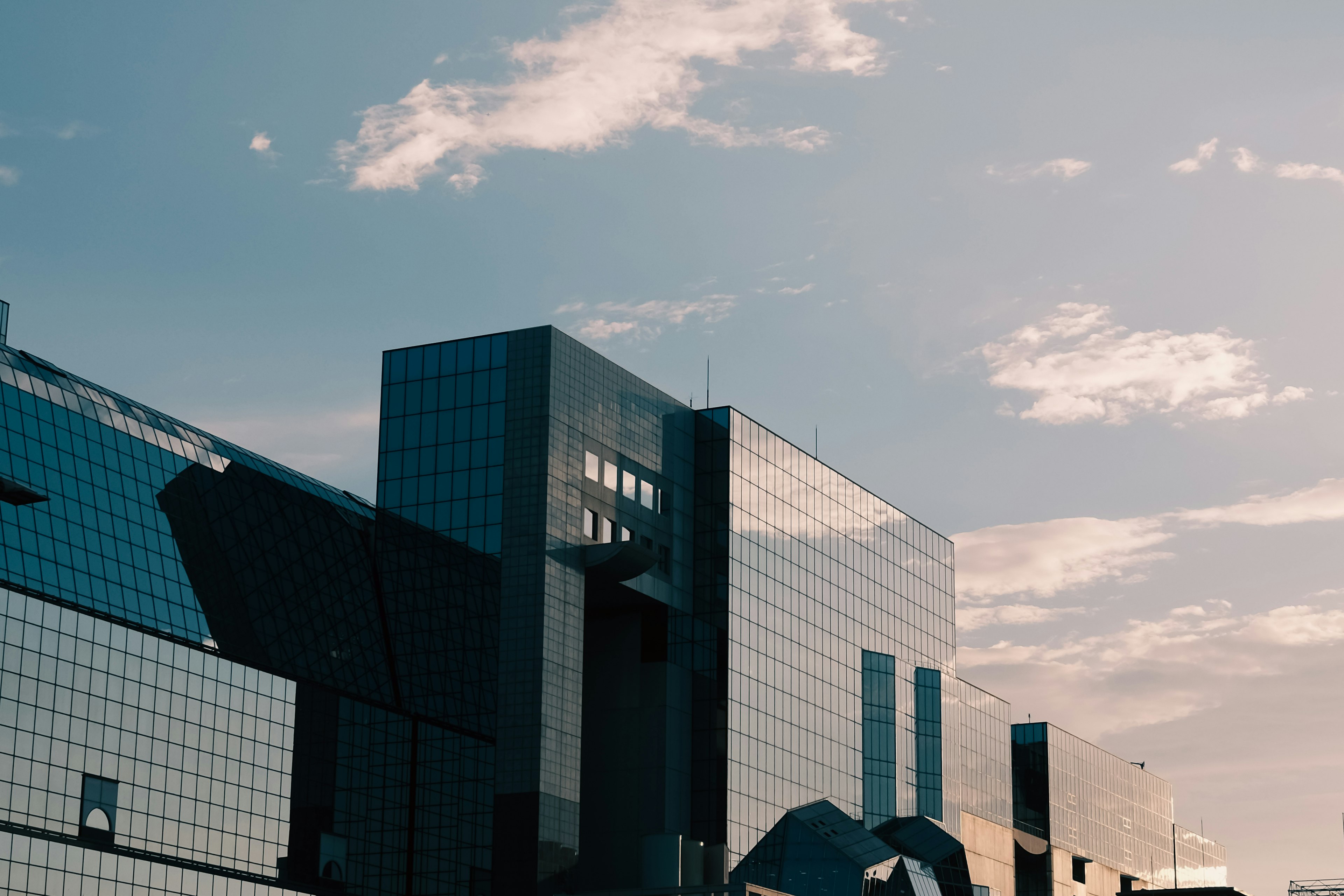 Part of a modern building under a blue sky with a reflective glass facade