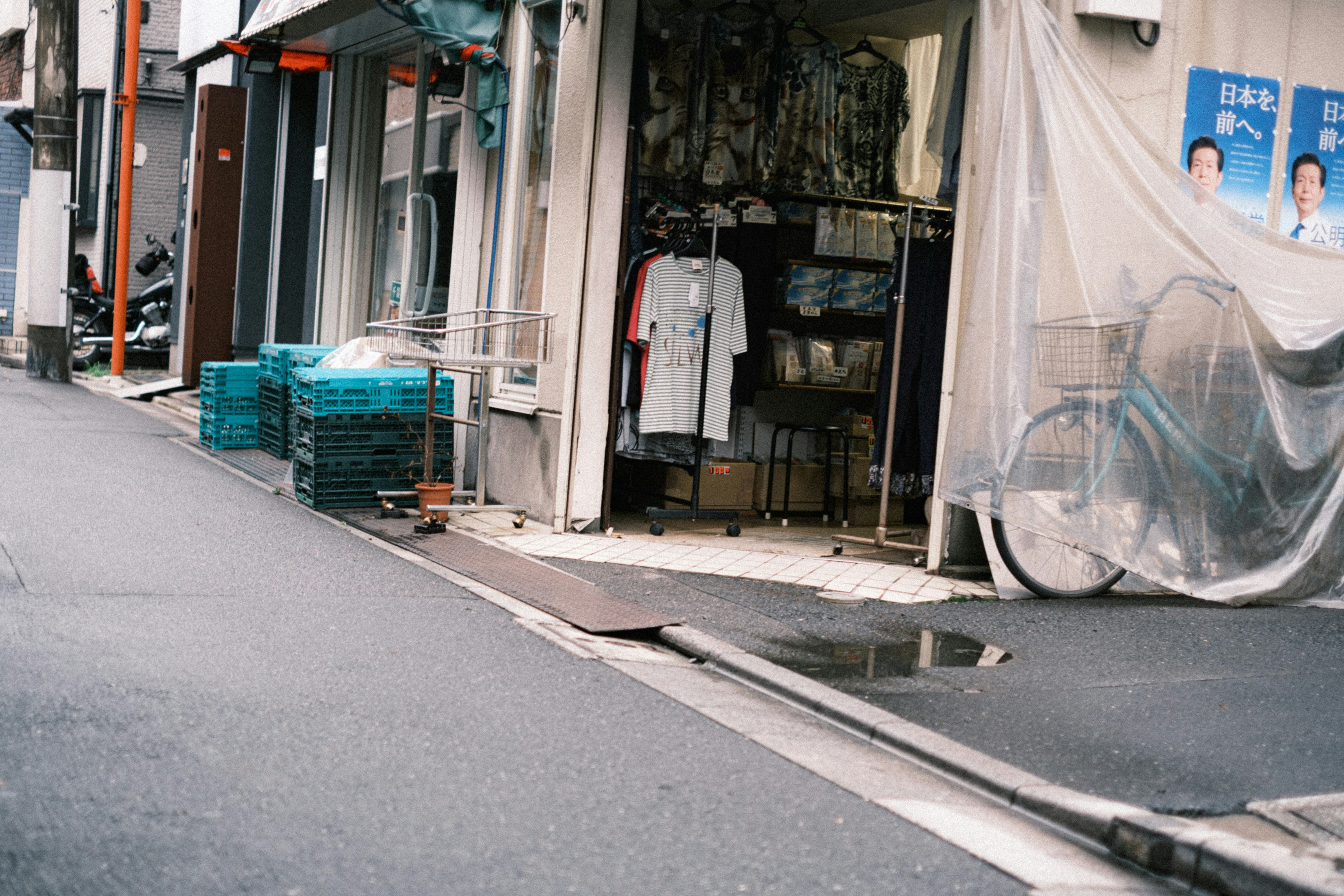 狭い路地にある店舗の外観と青いプラスチック製のコンテナ