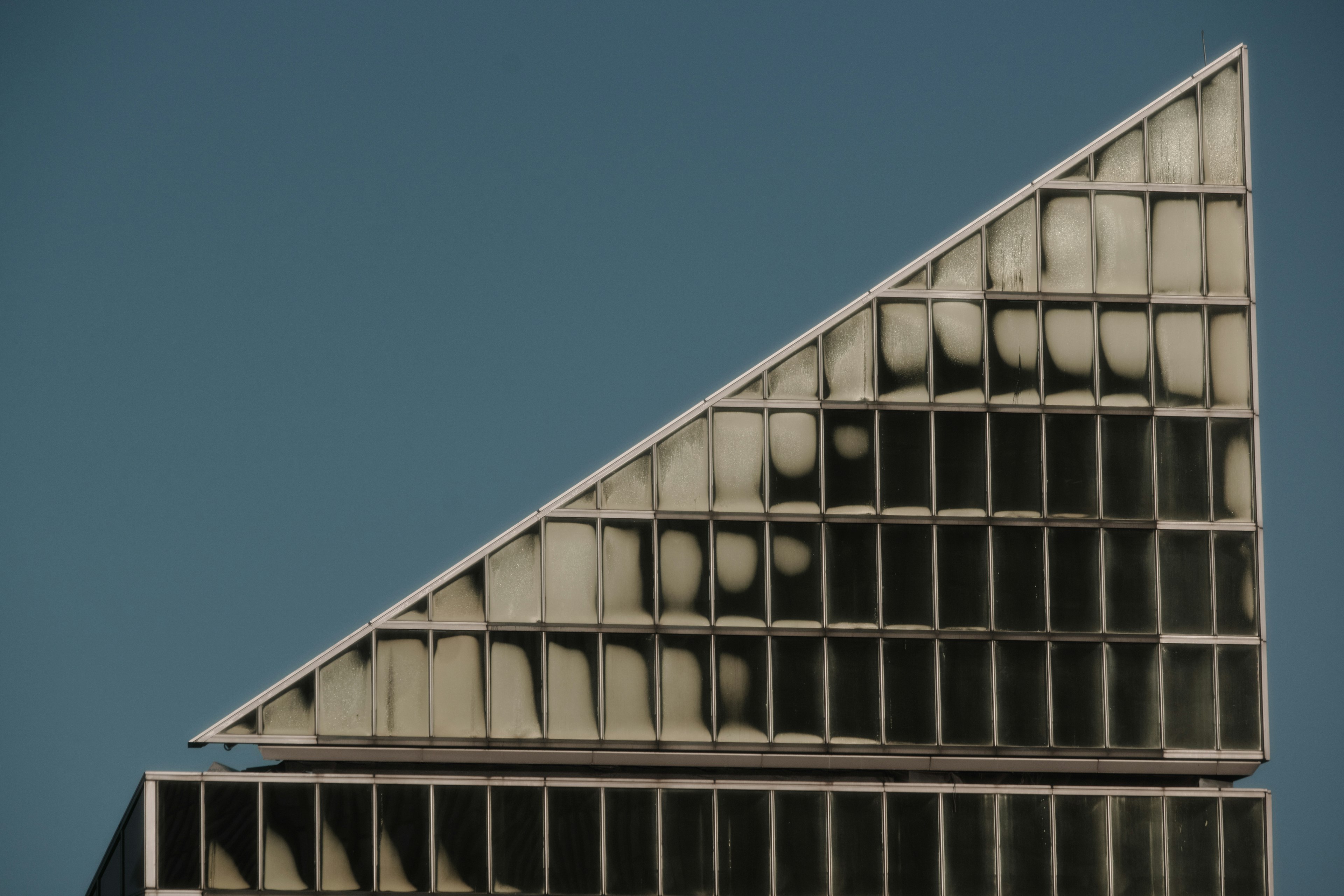 Parte superior de un edificio de vidrio triangular contra un cielo azul