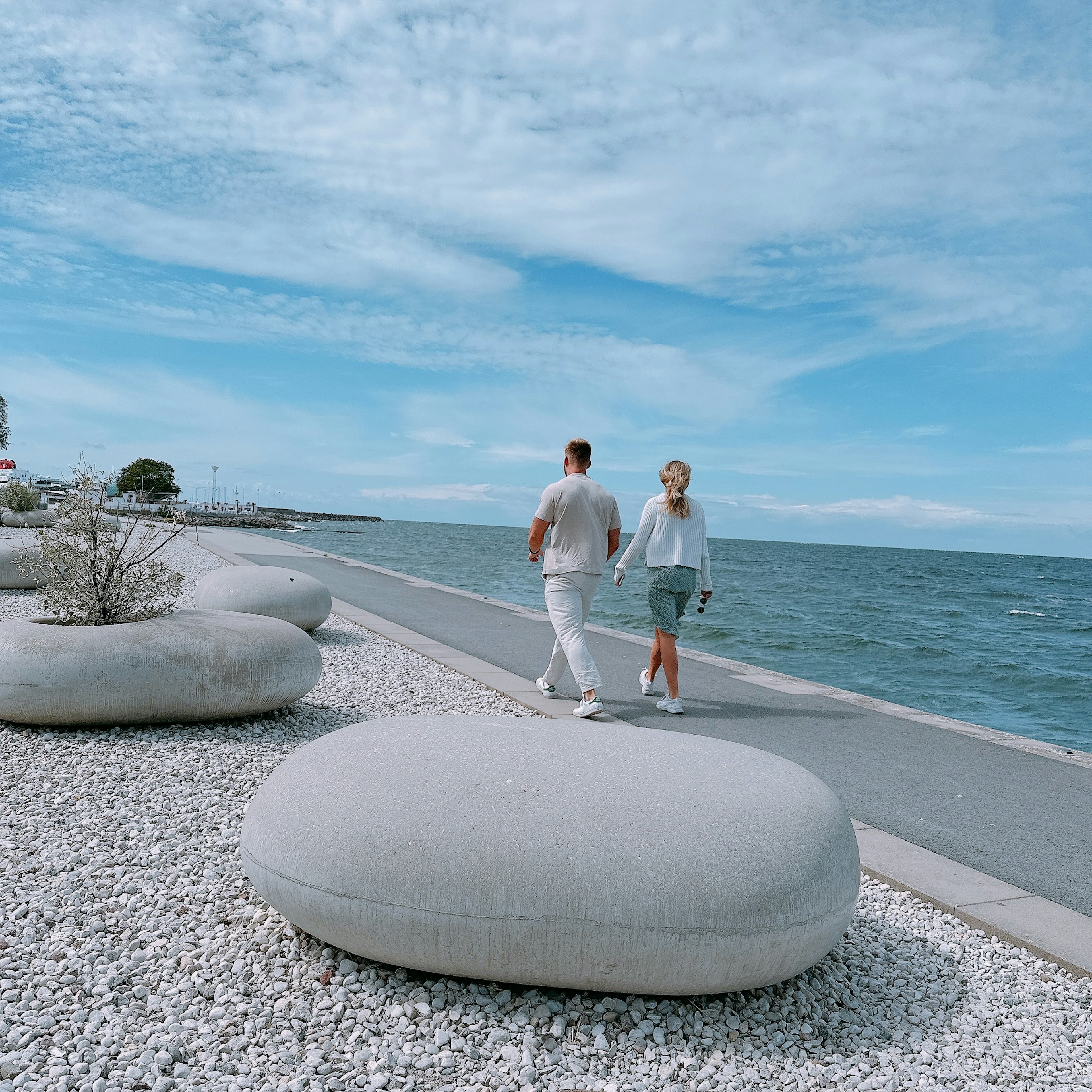 Pareja caminando por un camino costero con grandes piedras redondeadas y océano azul