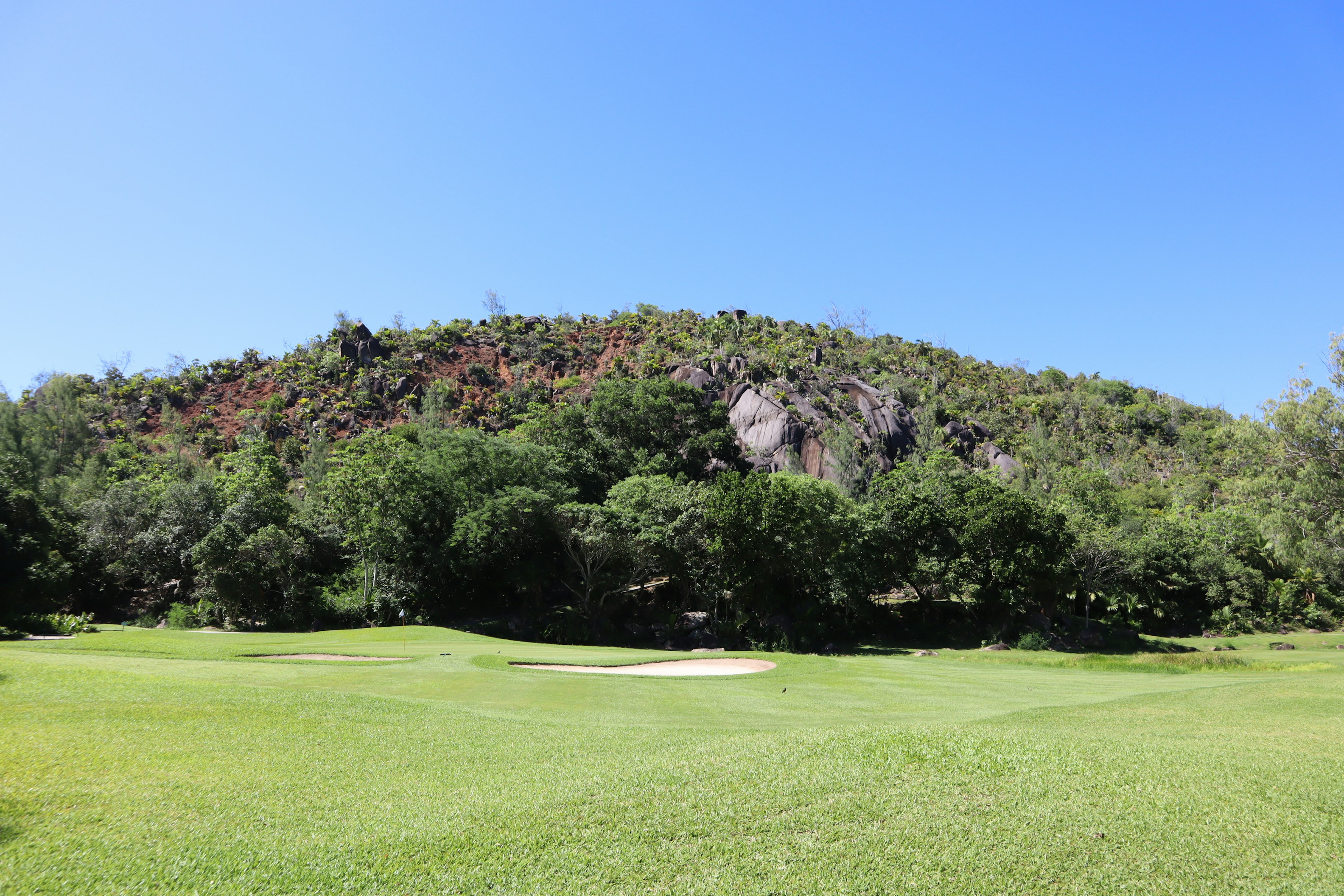 Paesaggio di un campo da golf lussureggiante con una collina sotto un cielo blu chiaro