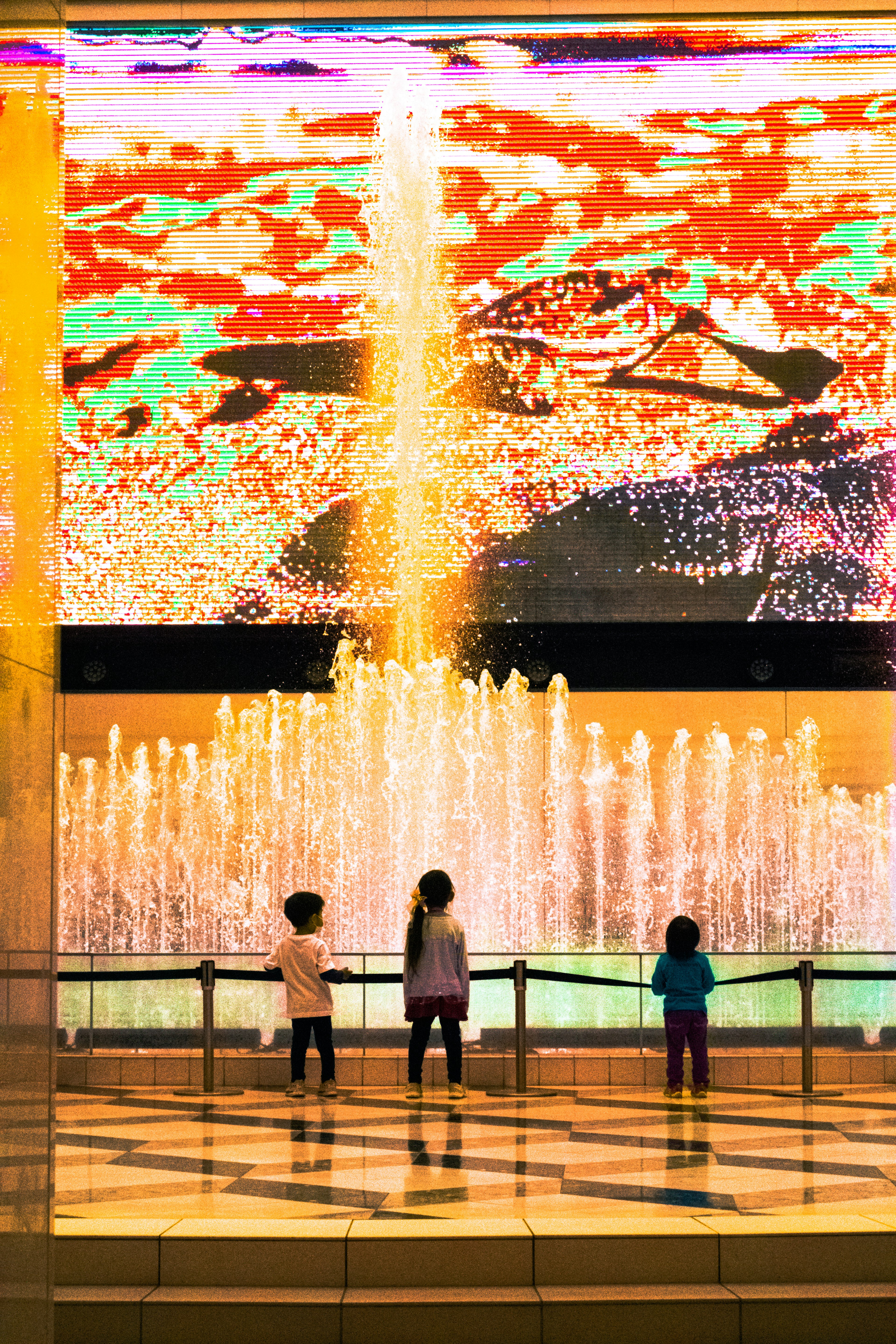 Children standing in front of a colorful light display and fountain