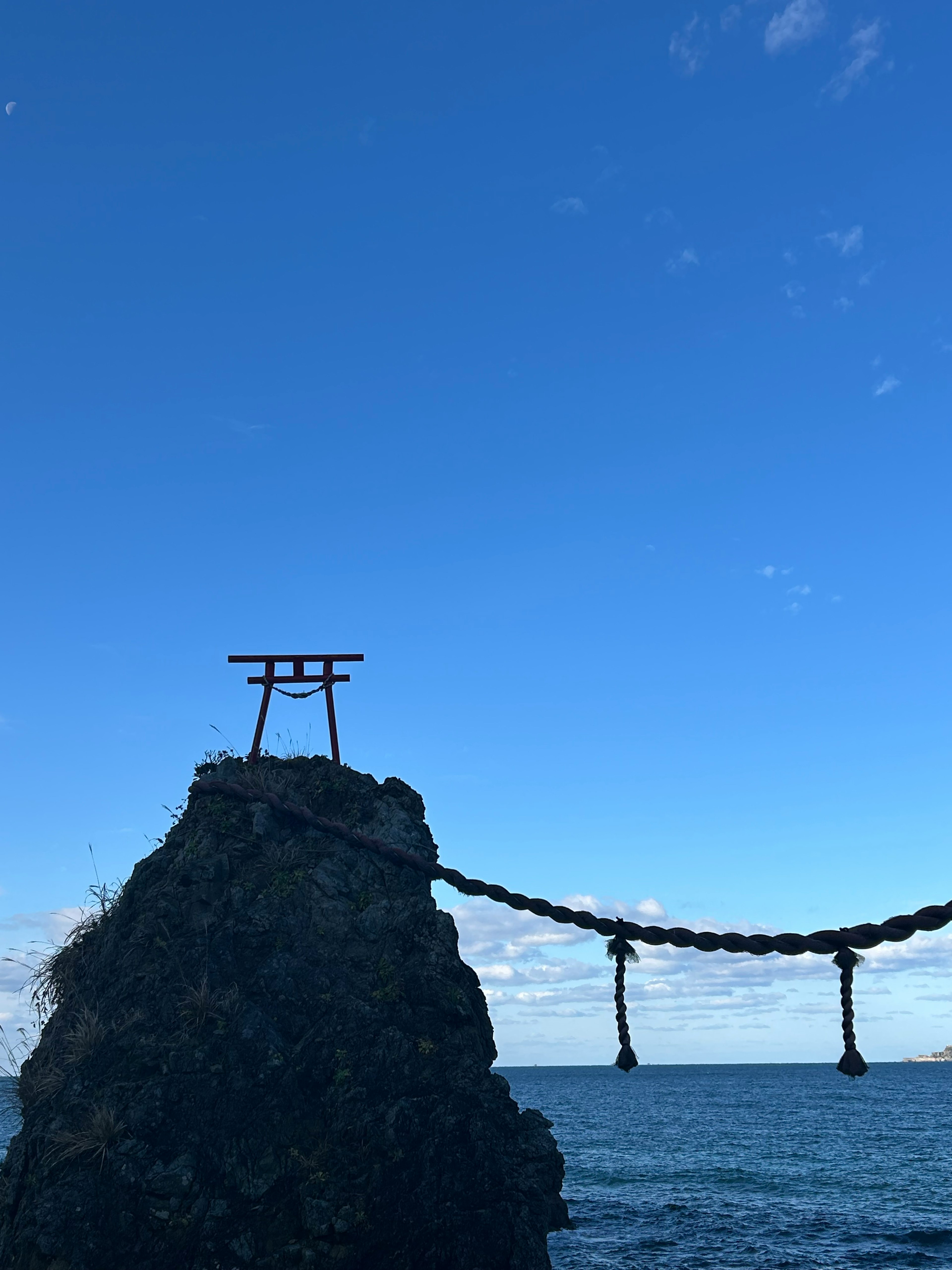 Torii gate on a rock above the sea with a large rope bridge