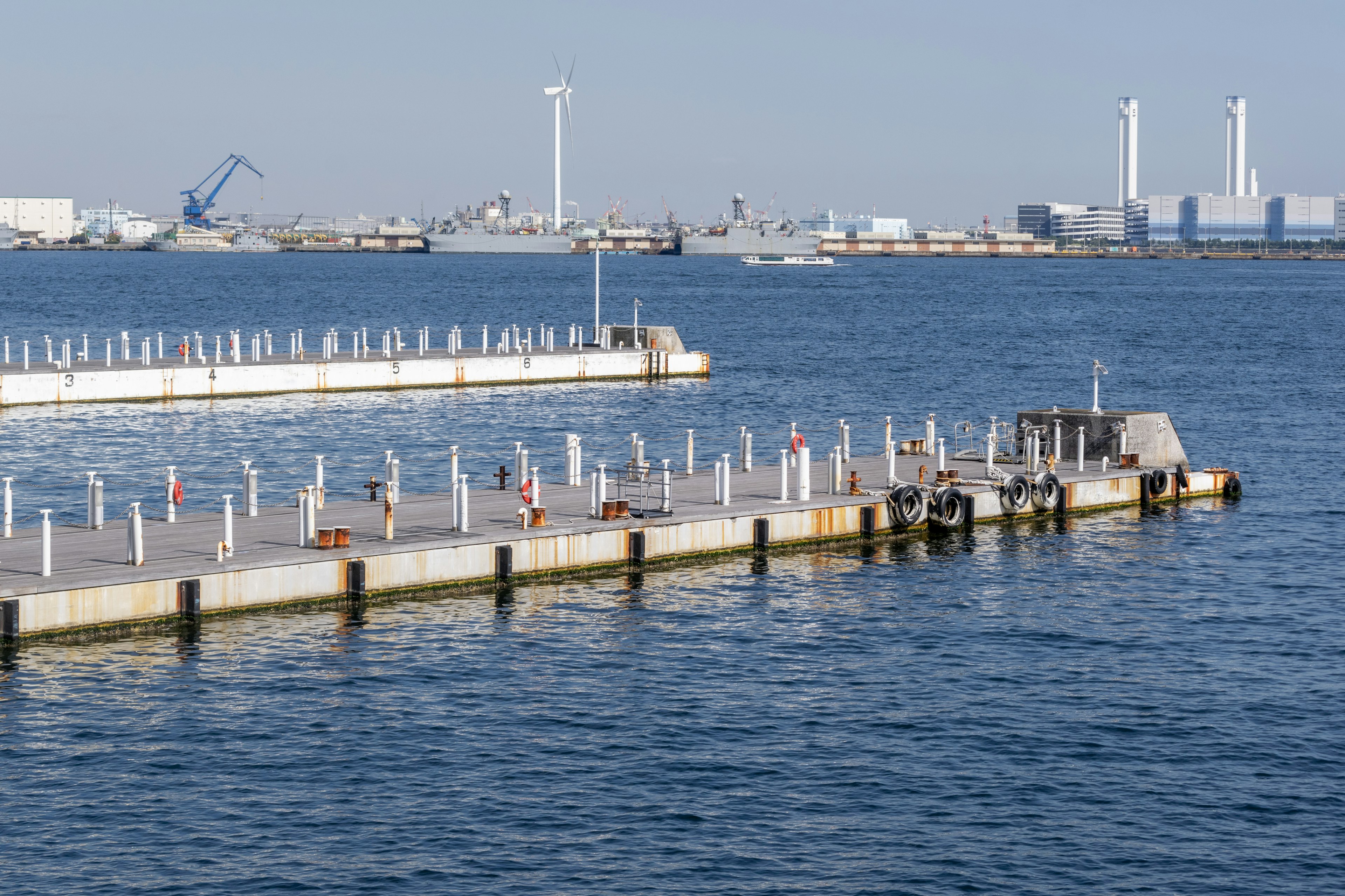 View of a dock on the water with industrial structures in the background