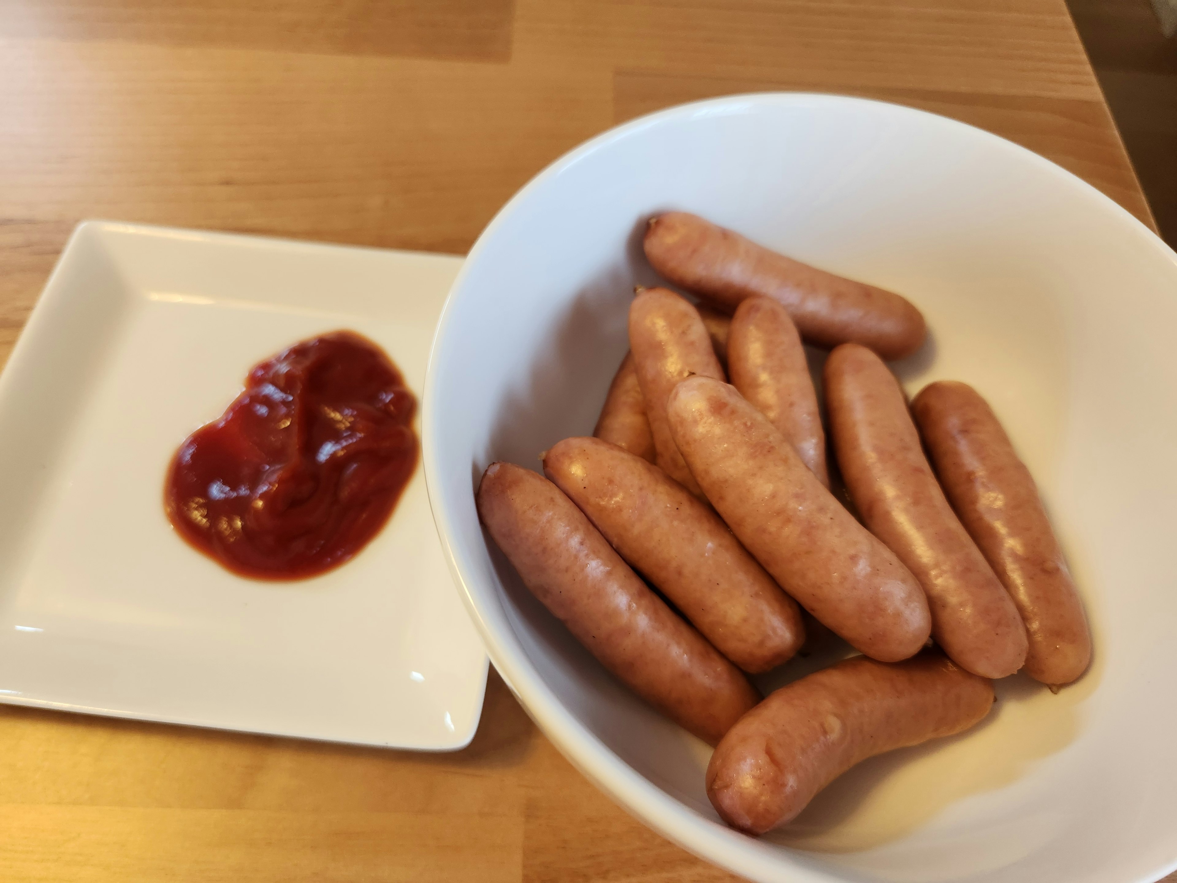 Sausages in a white bowl with ketchup on a small plate