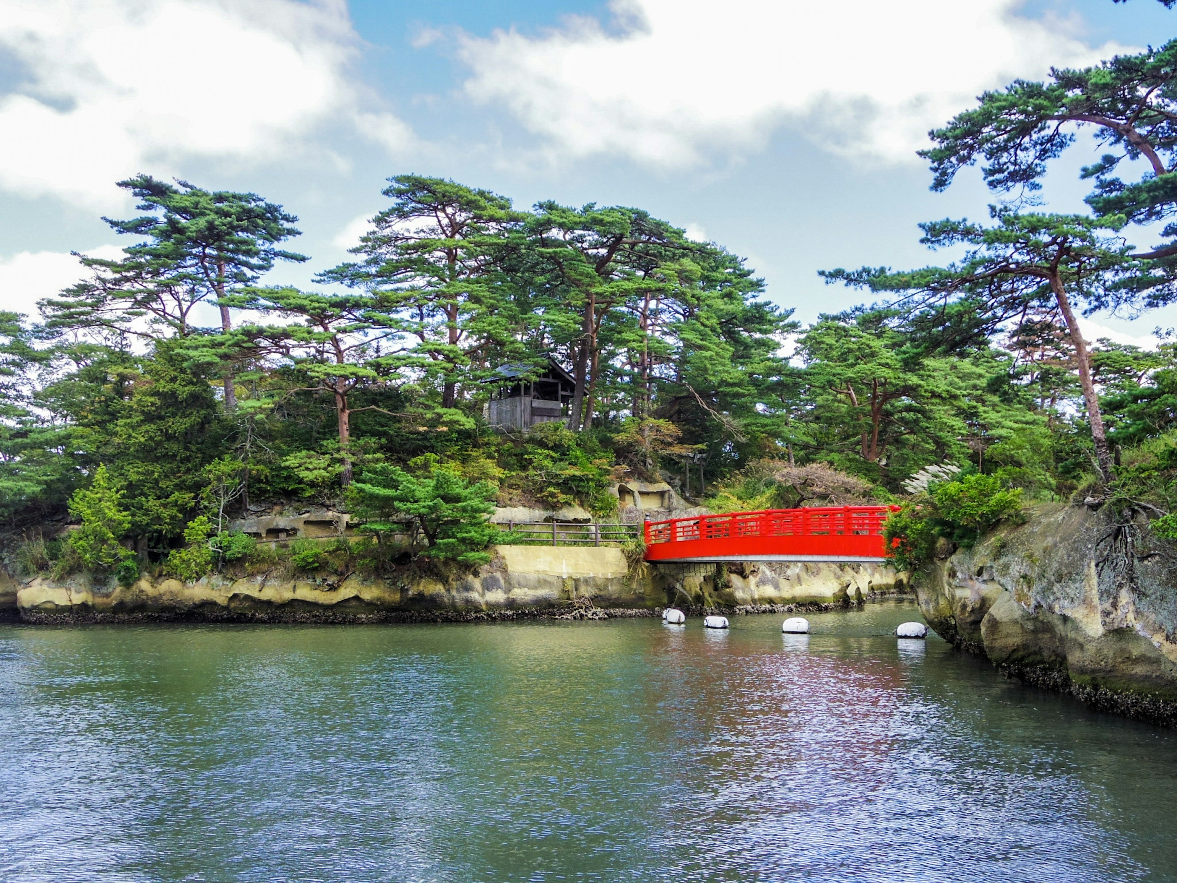 緑の木々に囲まれた赤い橋と静かな水面の風景