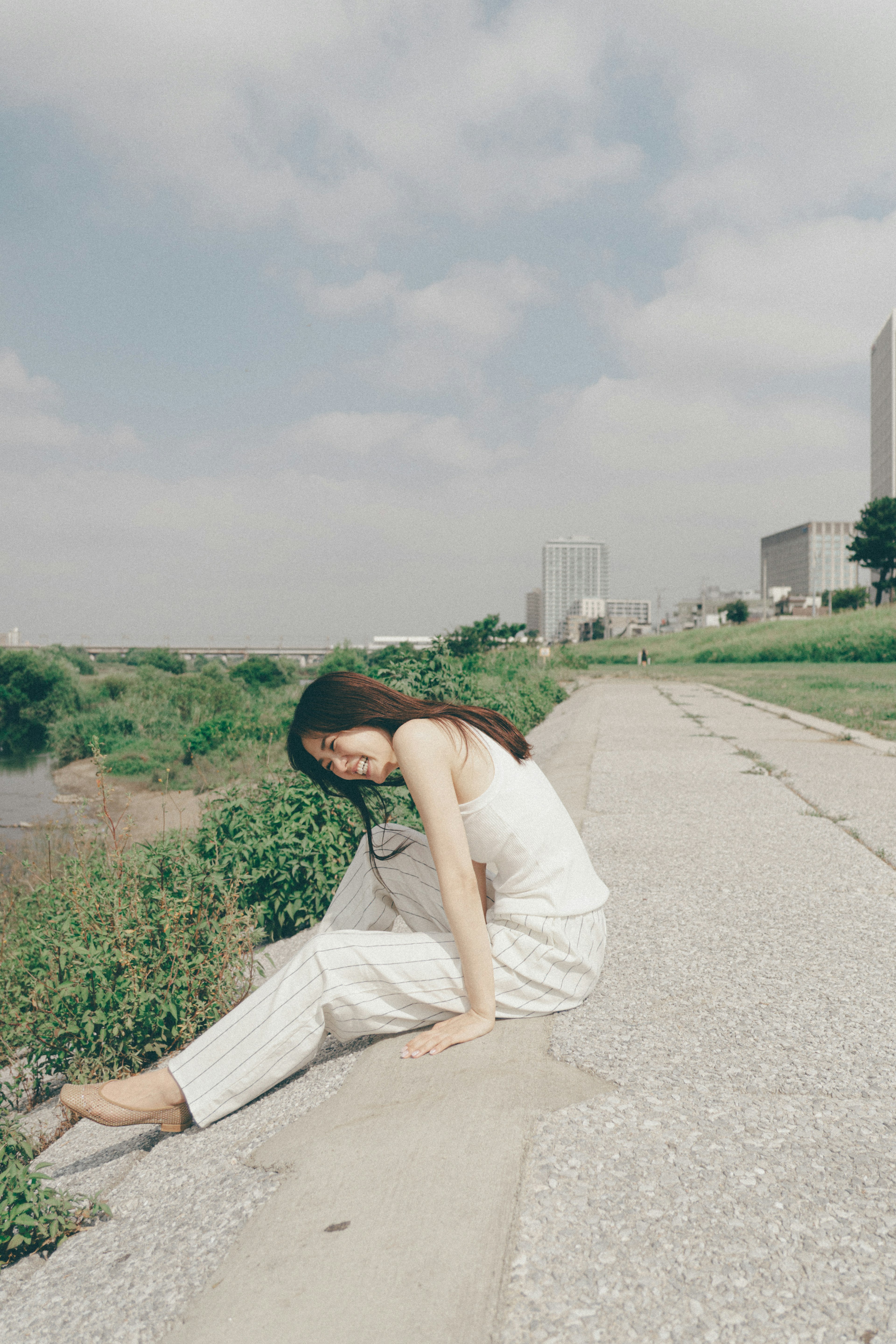 A woman in white clothing sitting by the river on a pathway