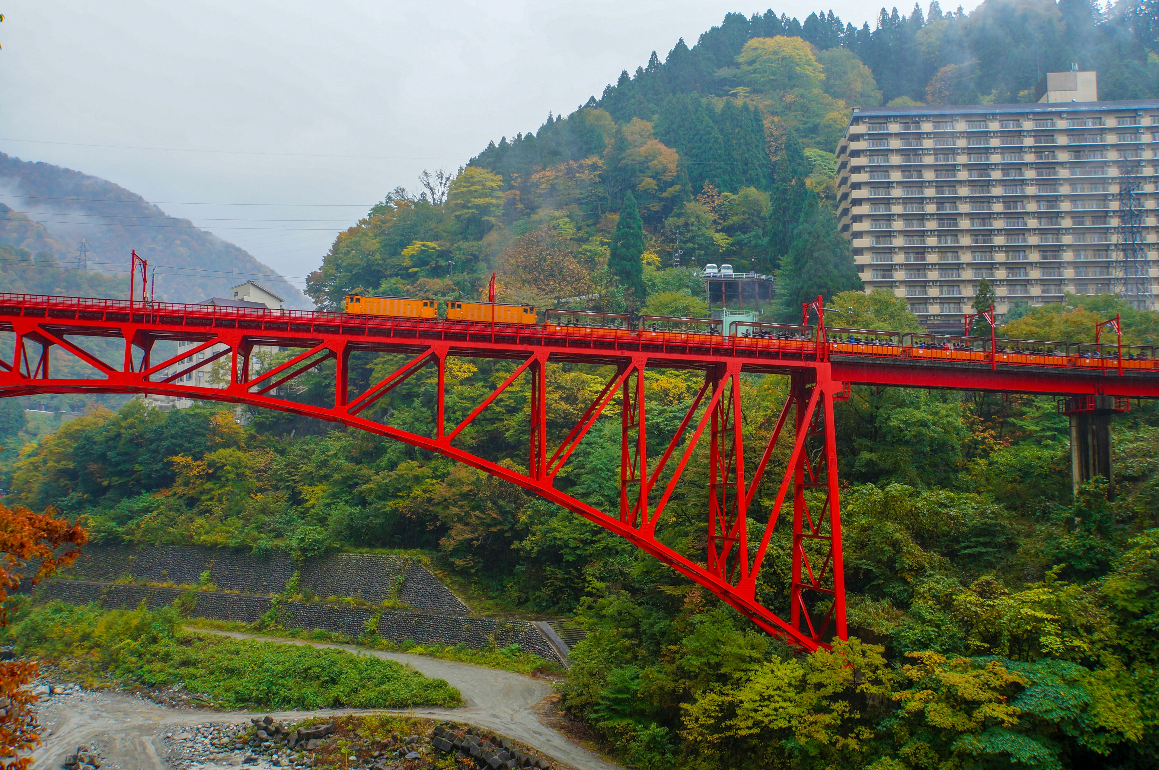 Roter Bogenbrücke mit herbstlichem Laub und Hotel im Hintergrund