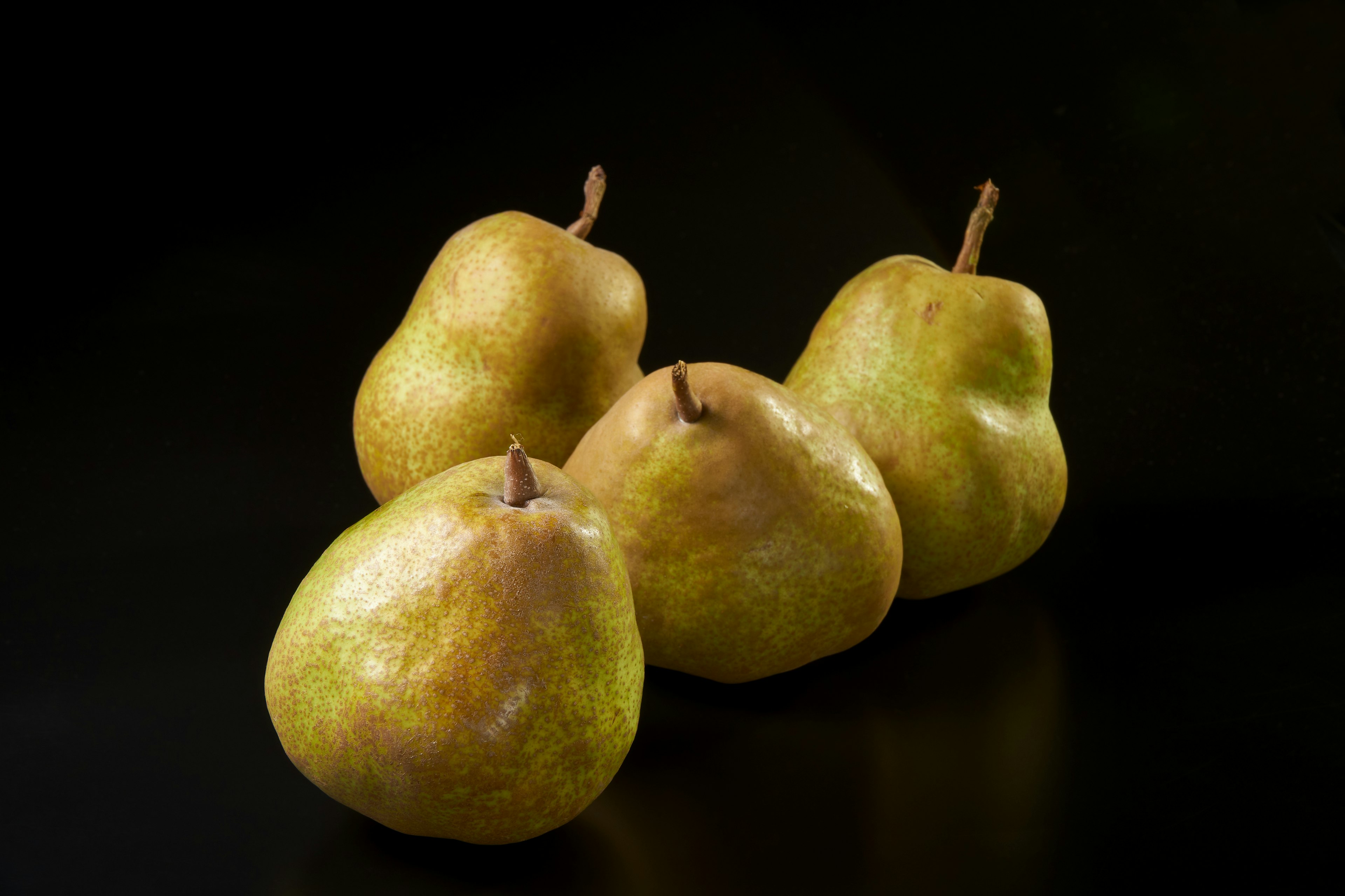 Four yellow pears arranged on a black background