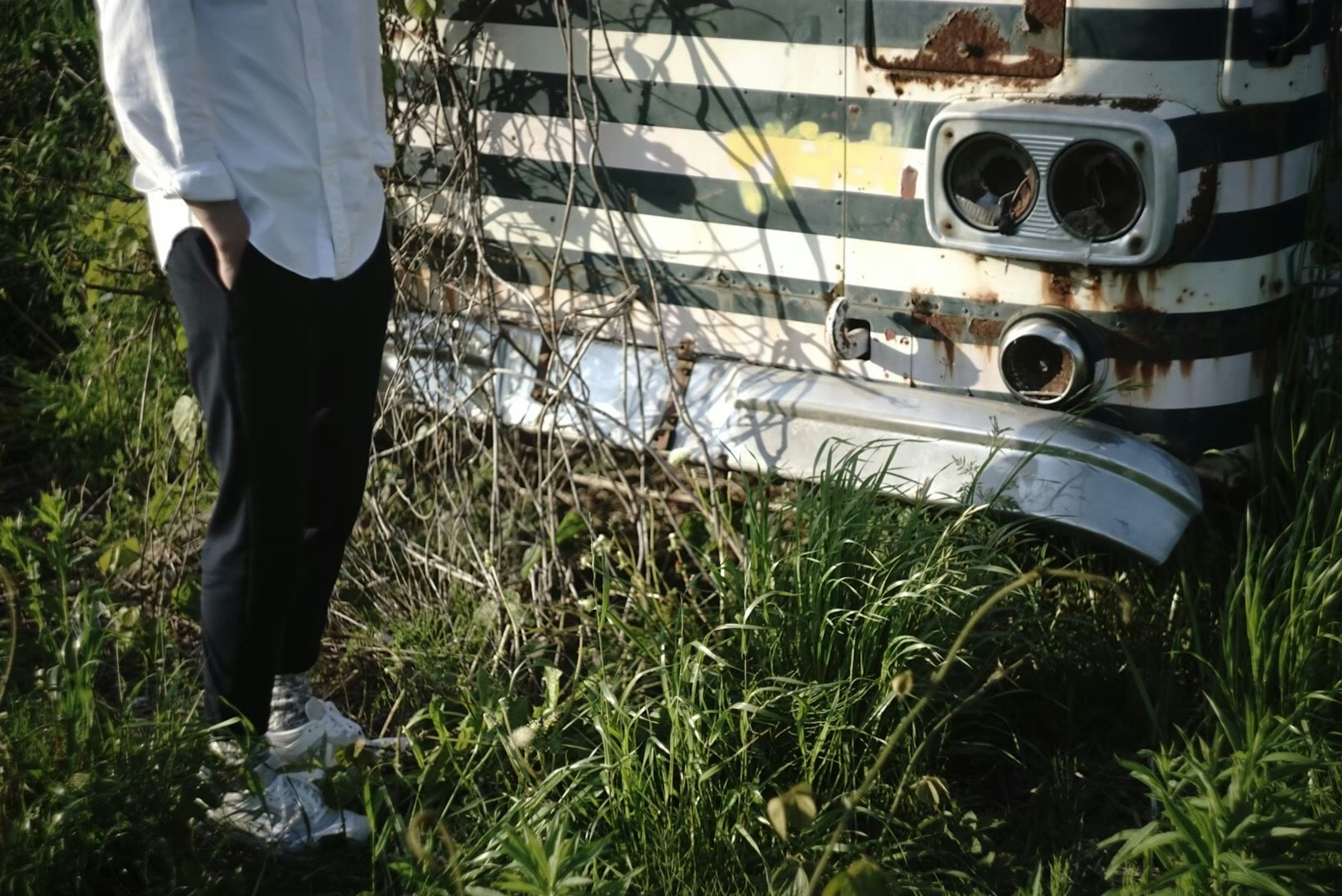 Person standing next to an old bus covered in grass