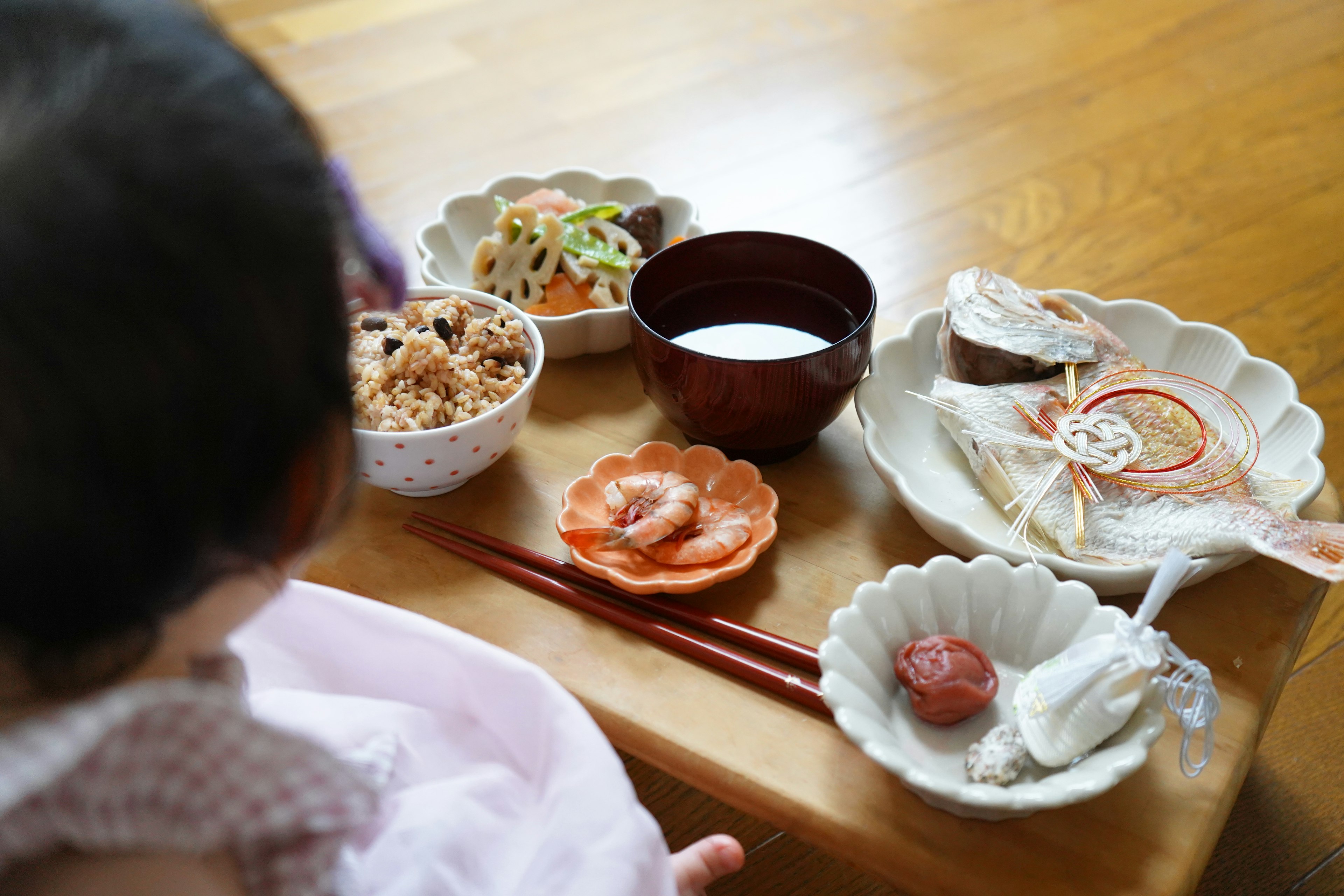 A baby sitting at a table with a traditional Japanese meal