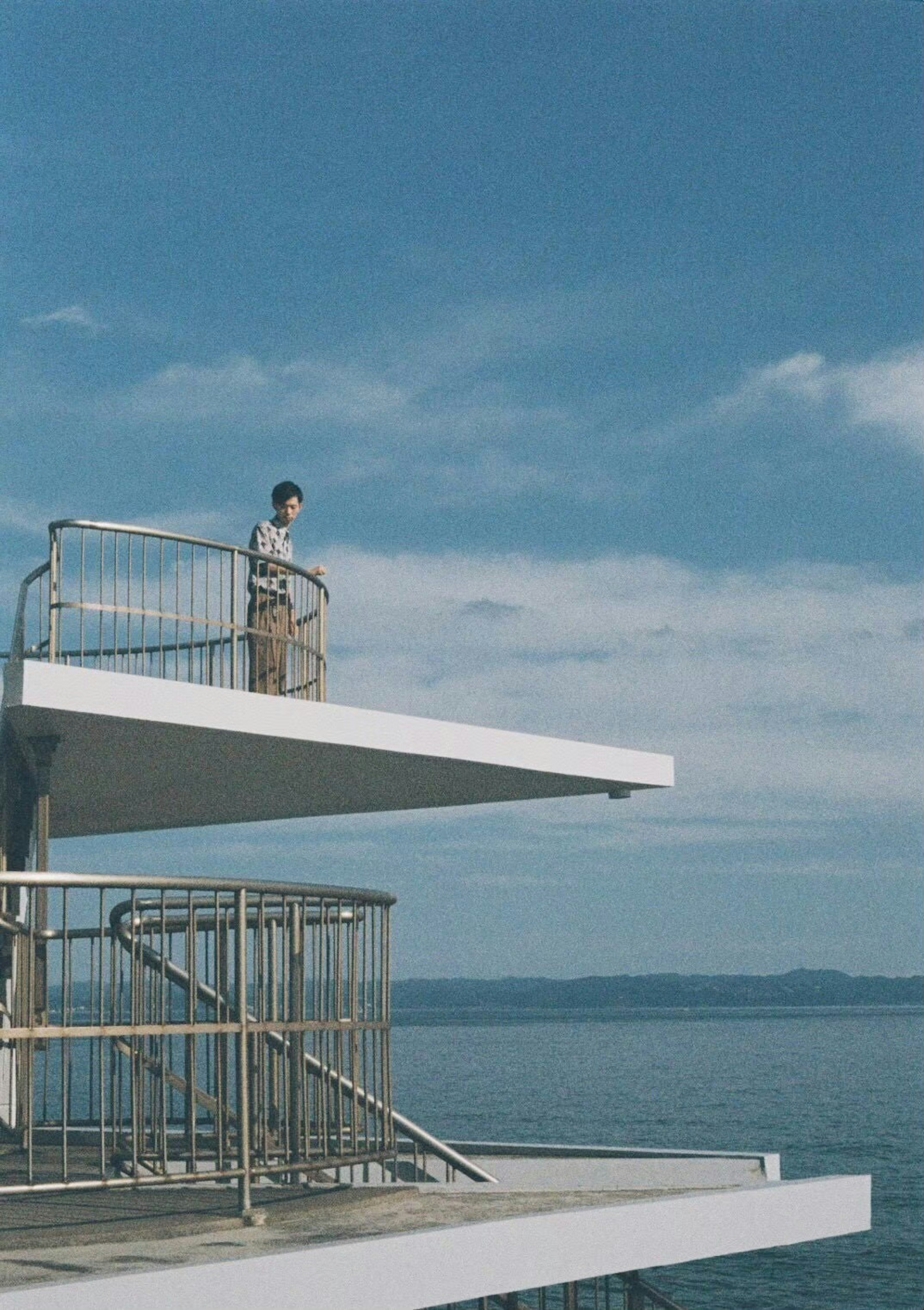 A boy standing on a diving platform overlooking the blue sea and sky