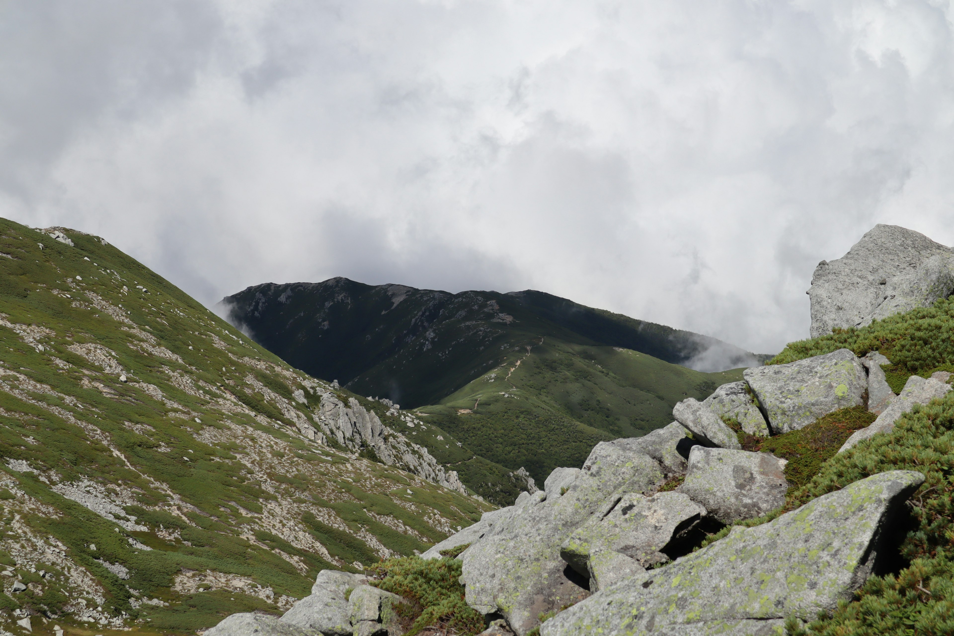 山脈和雲彩的風景，綠丘上的岩石