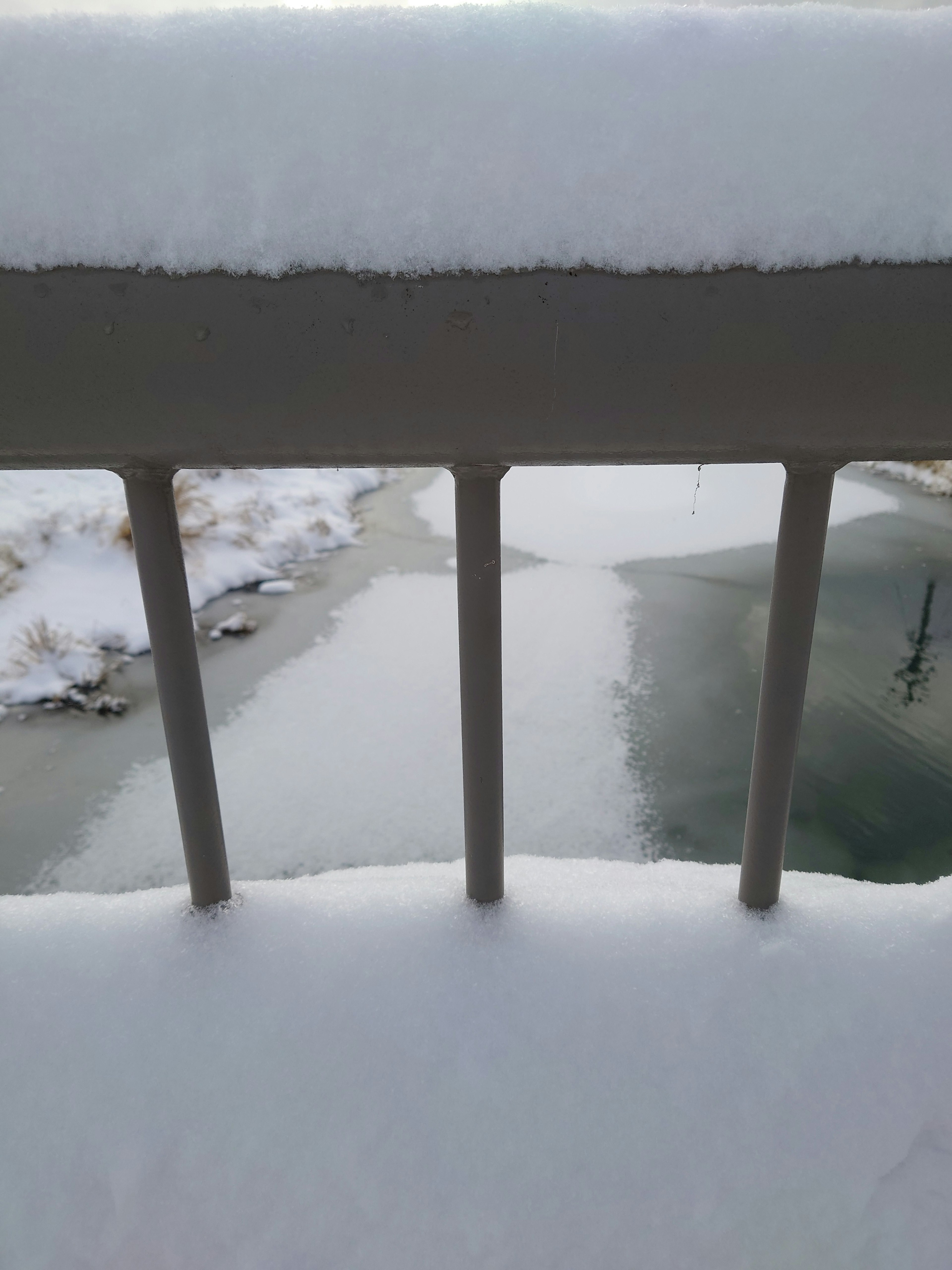 Snow-covered railing overlooking a frozen surface of water