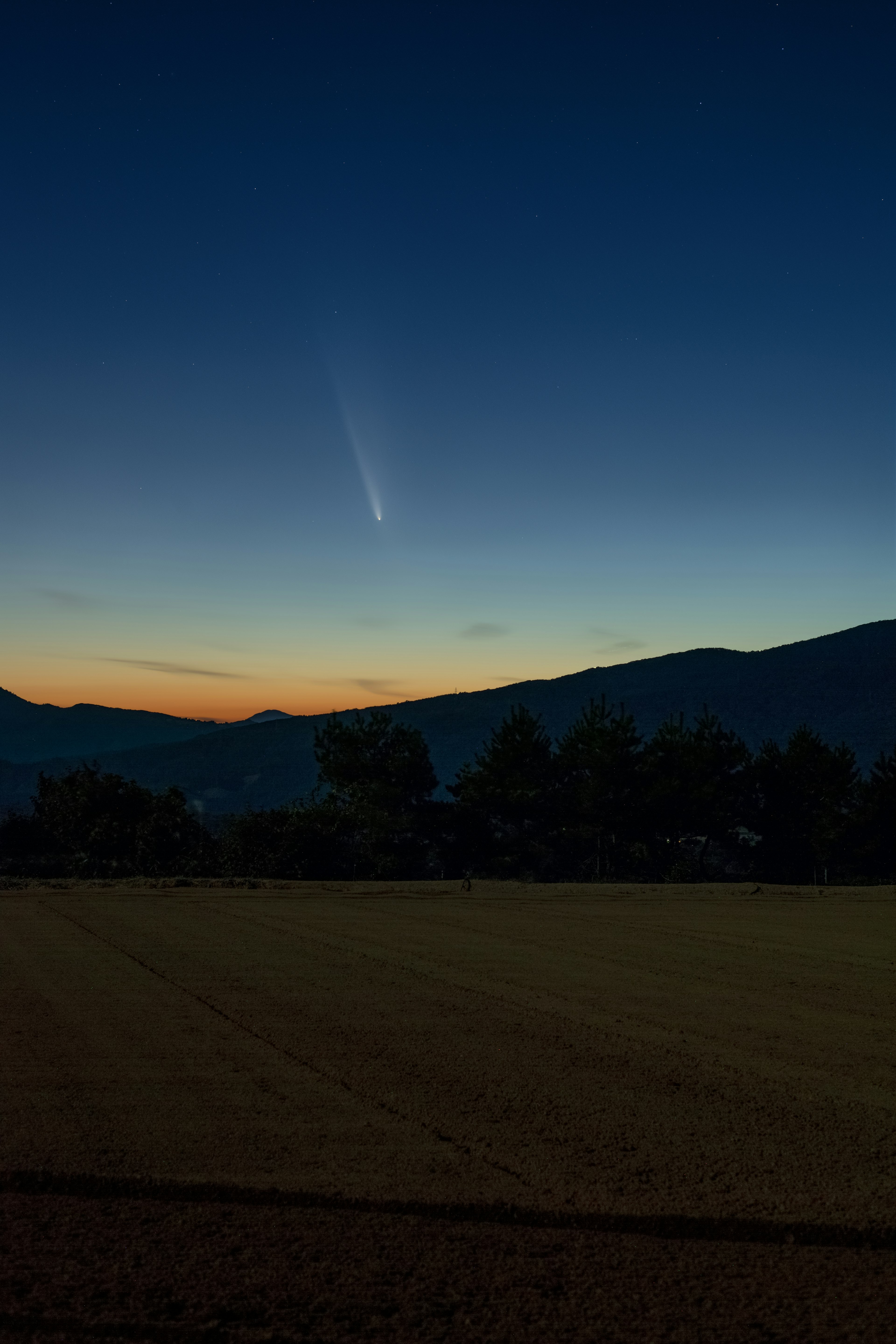 夕暮れの空に現れる彗星と山々のシルエット