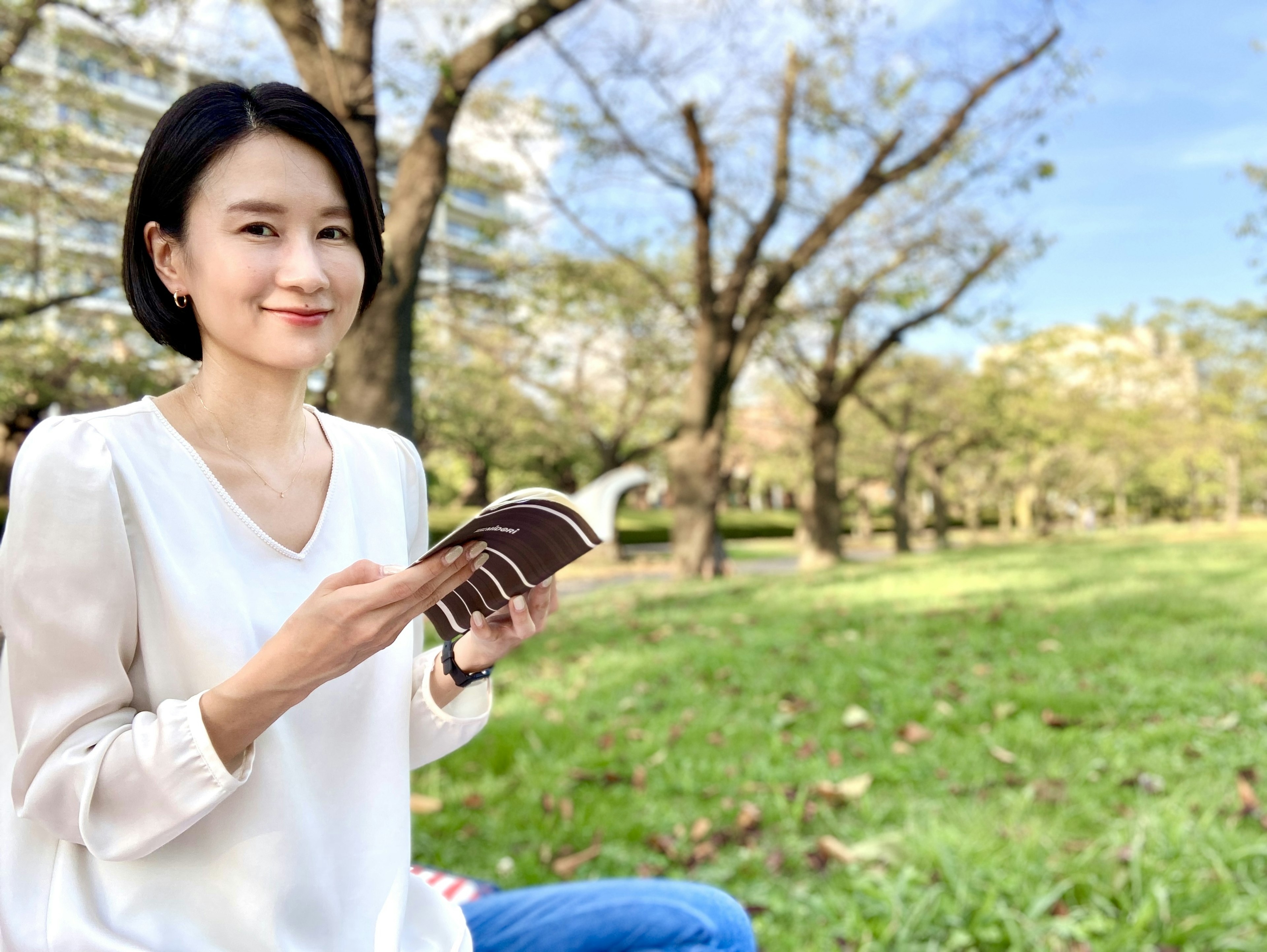 Woman smiling while reading a book in a green park