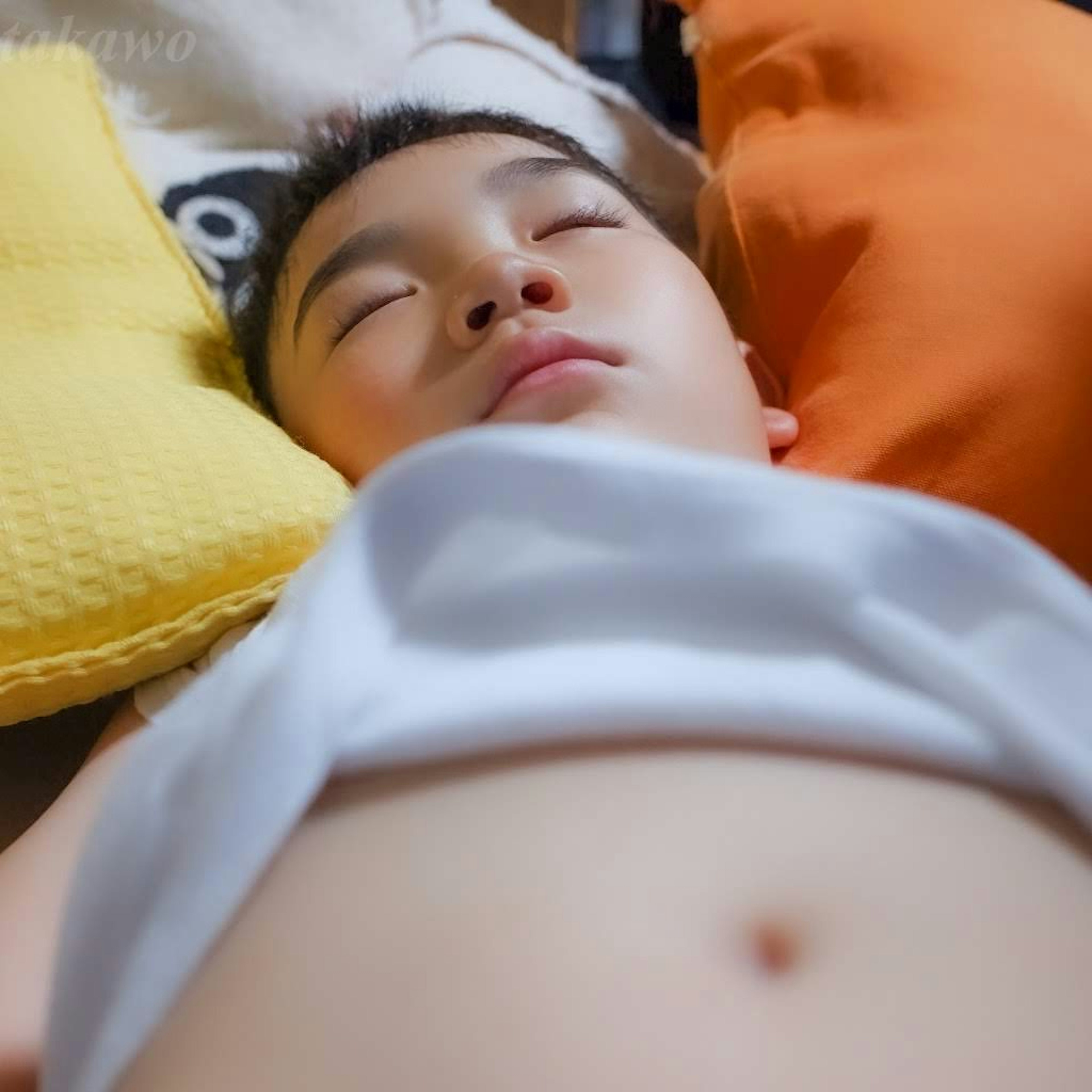 A boy sleeping in a white shirt surrounded by yellow and orange cushions