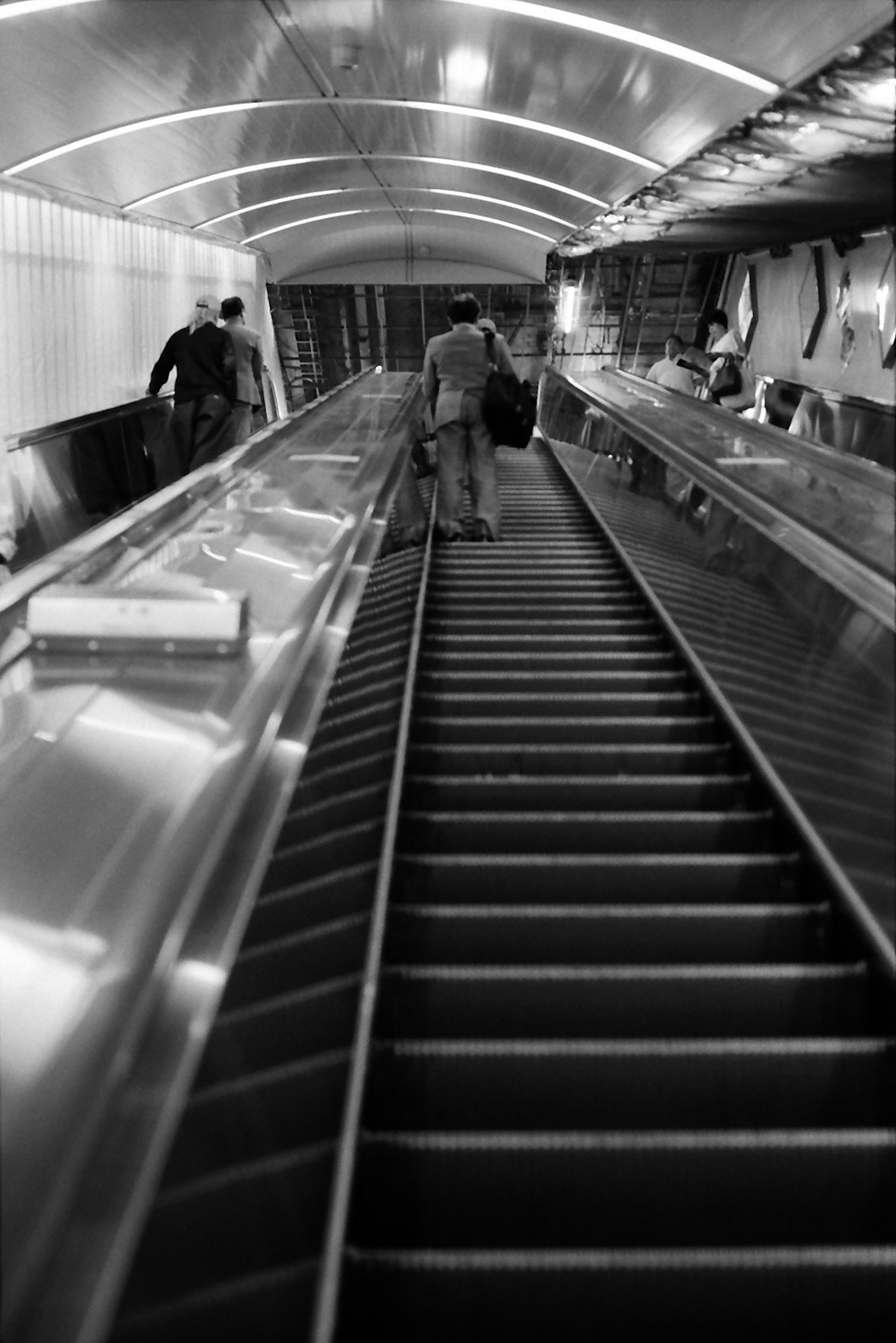 Black and white photo of people descending a subway escalator