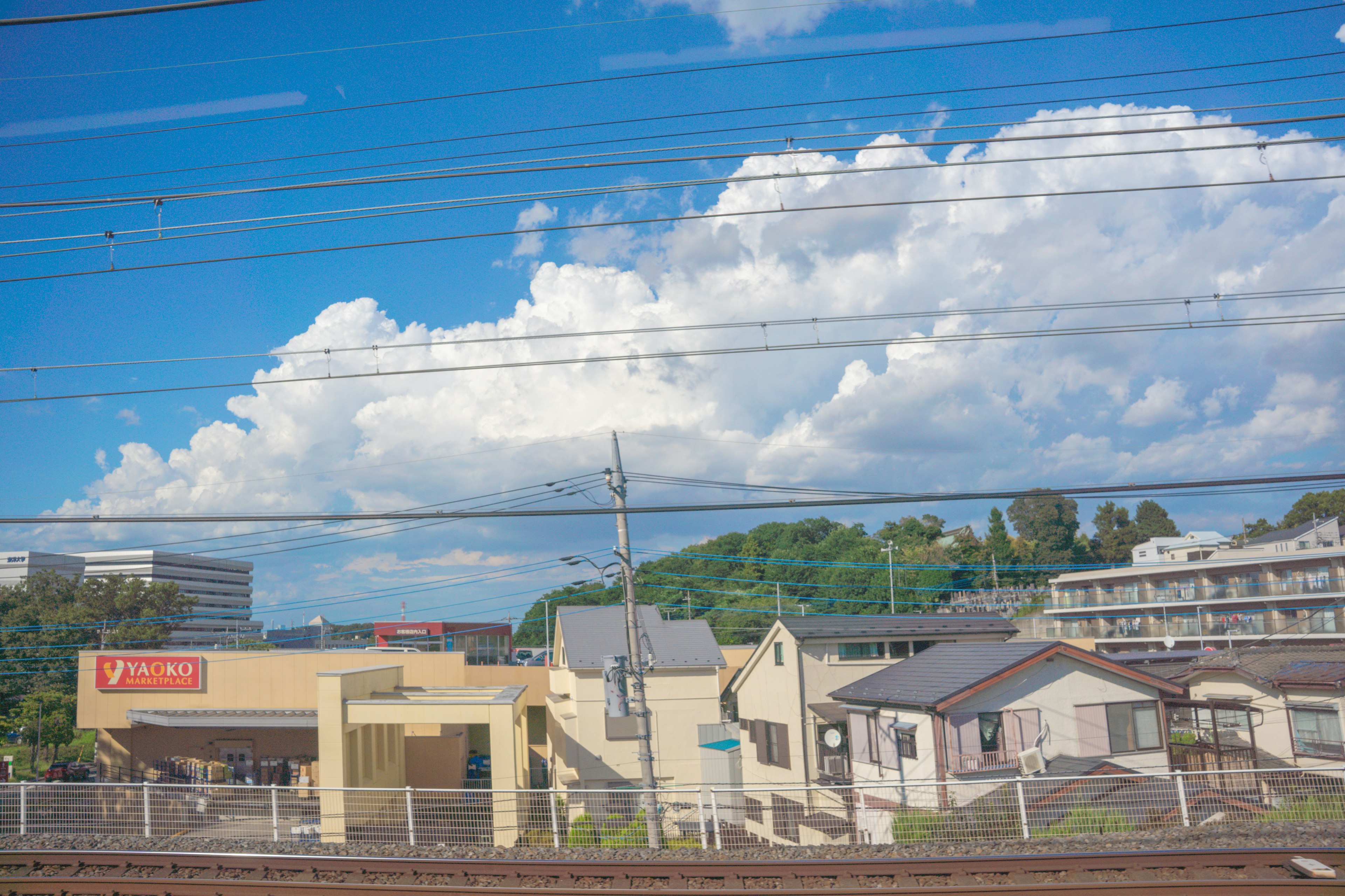 青空と白い雲が広がる風景に、鉄道線路沿いの建物が並ぶ