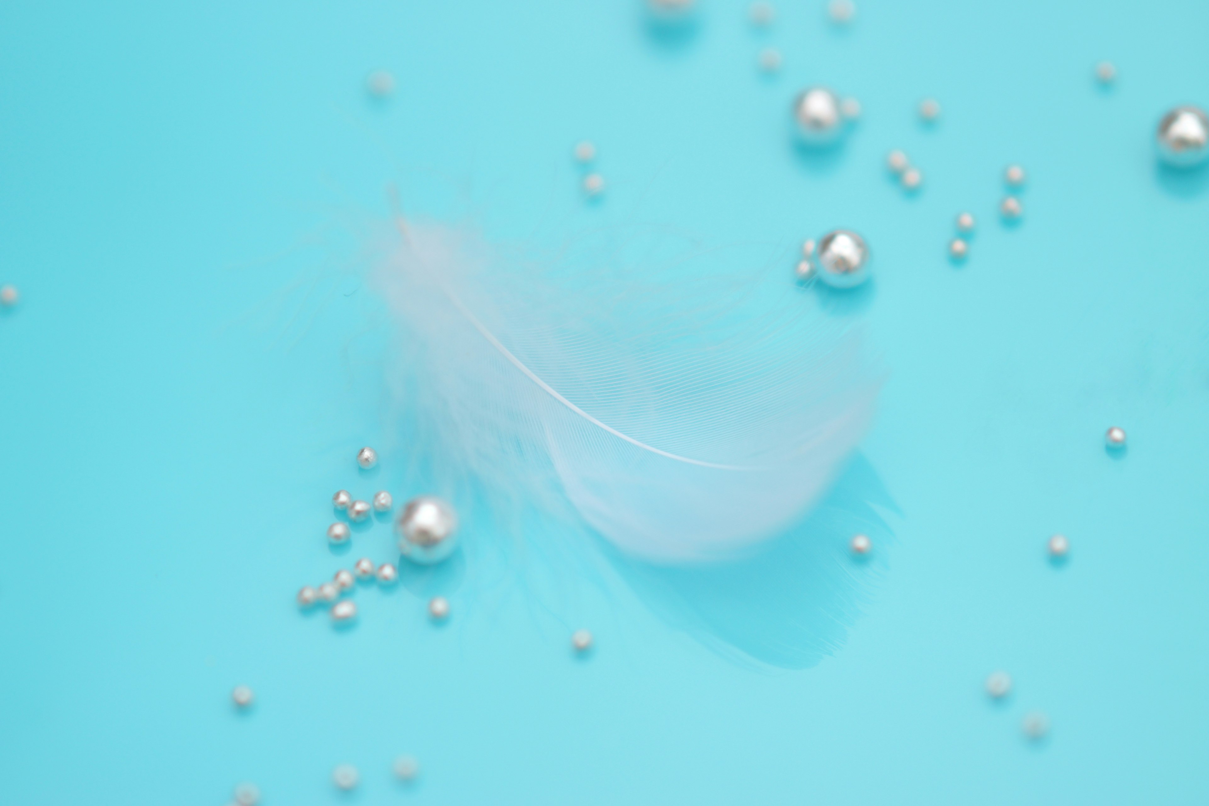 A white feather and scattered pearls on a blue background