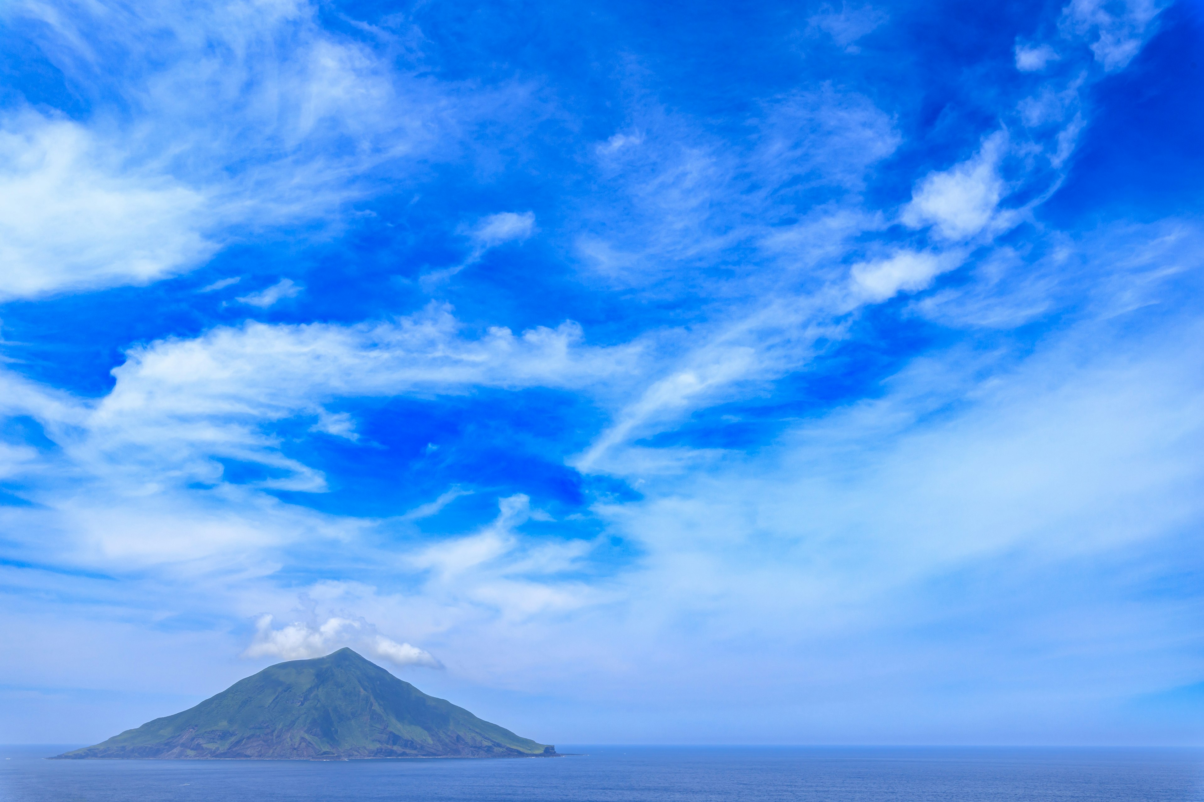 Un'isola verde circondata da un oceano blu calmo sotto un cielo blu brillante con nuvole bianche