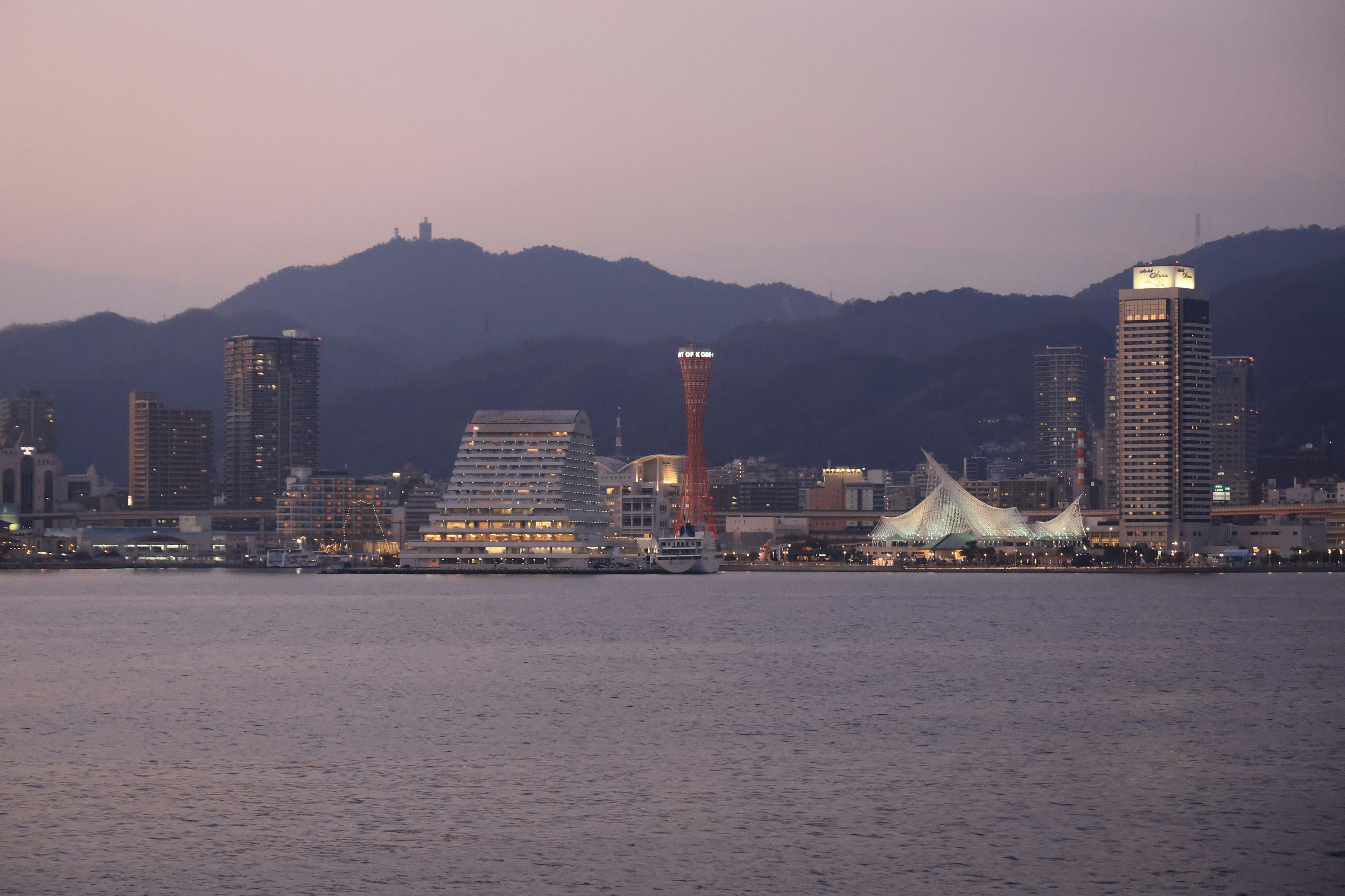 Vista nocturna de la ciudad de Kobe con rascacielos y montañas al otro lado del mar