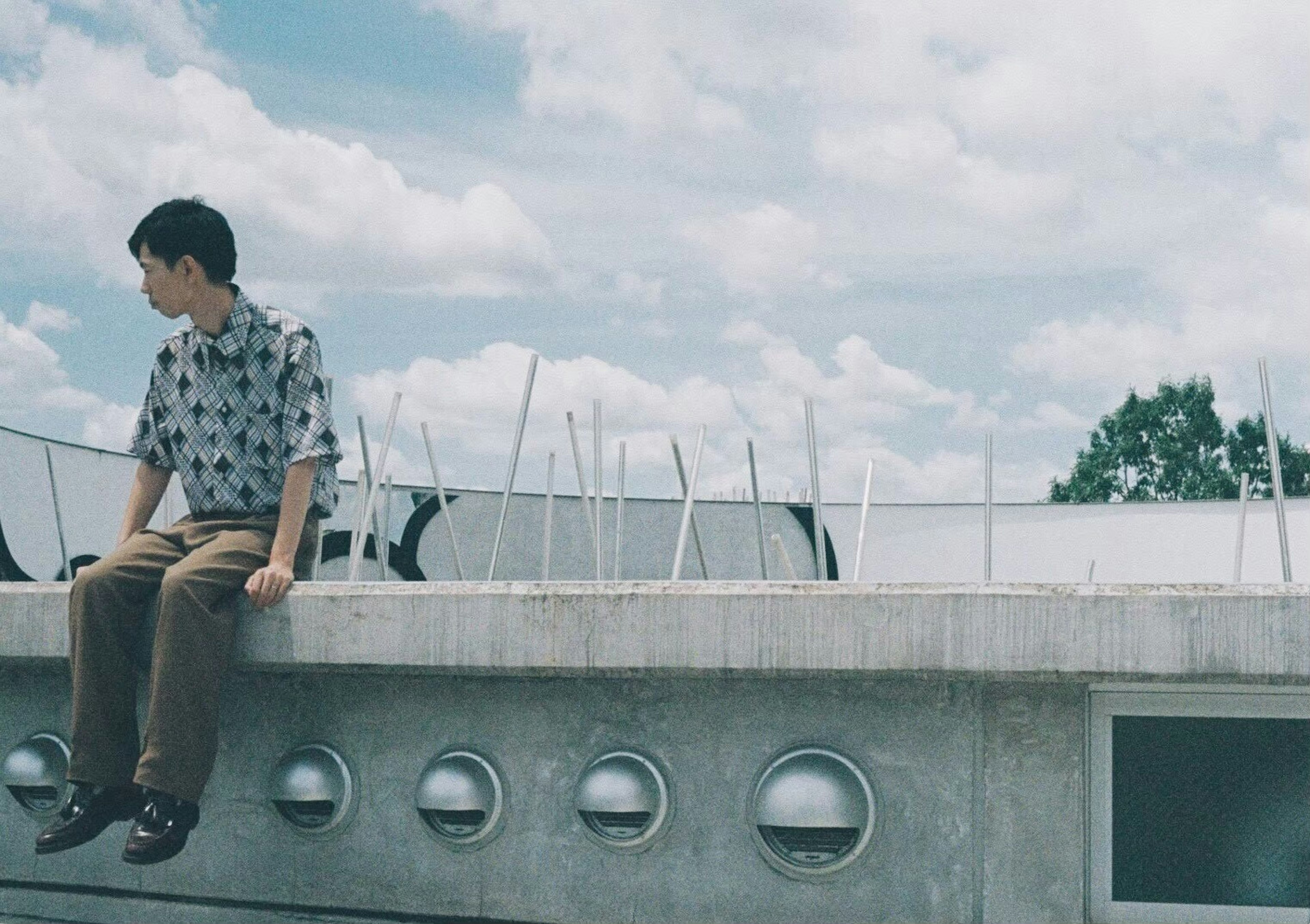 Young man sitting on a concrete wall under a blue sky